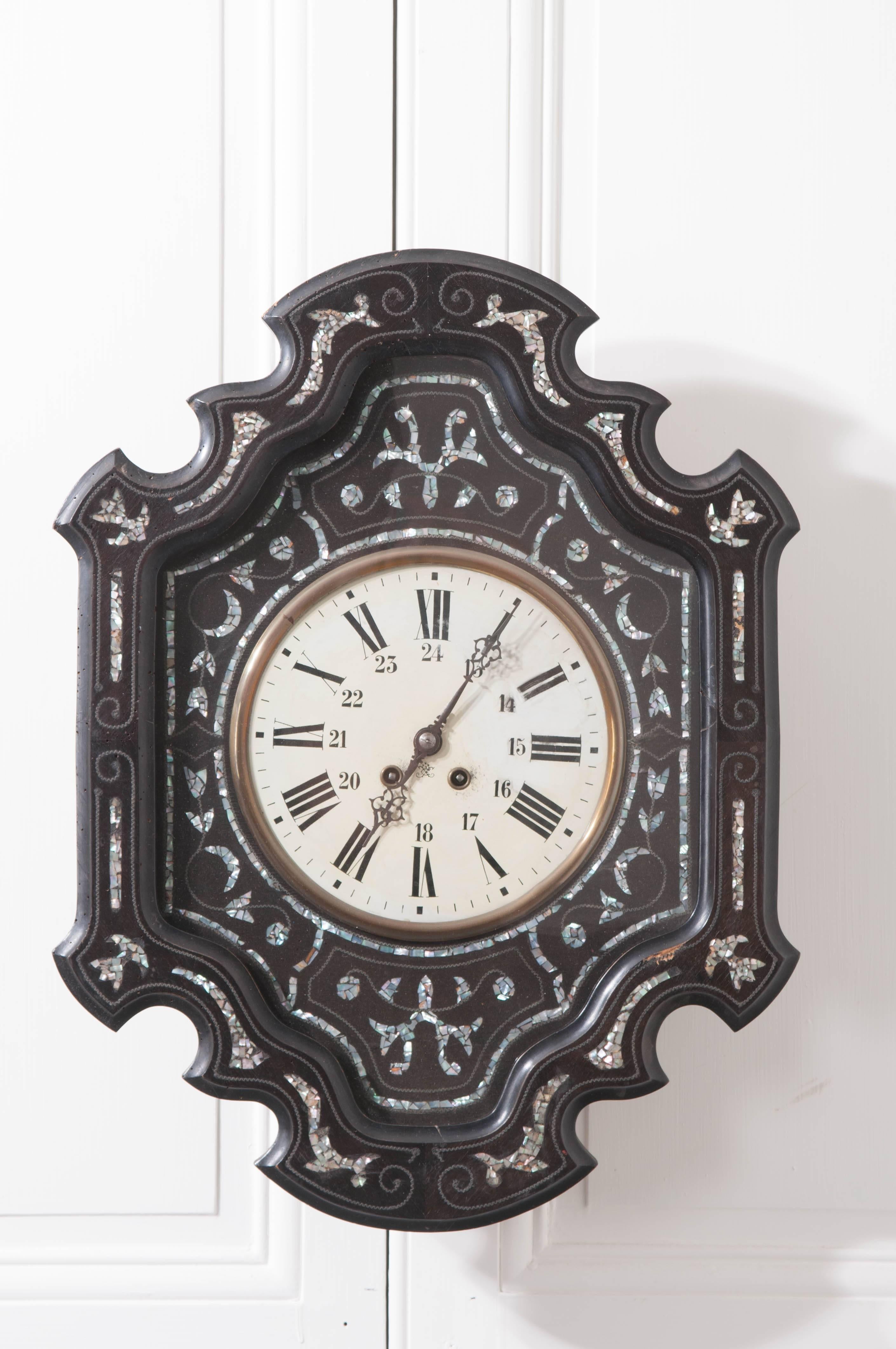 This 19th century clock is stunning with its rippling, shaped clock frame of ebonized wood. Mother-of-pearl designs are masterfully inlaid into the ebonized wood, surrounding the paper clock face in symmetrical forum. The scrolled forms of leaves