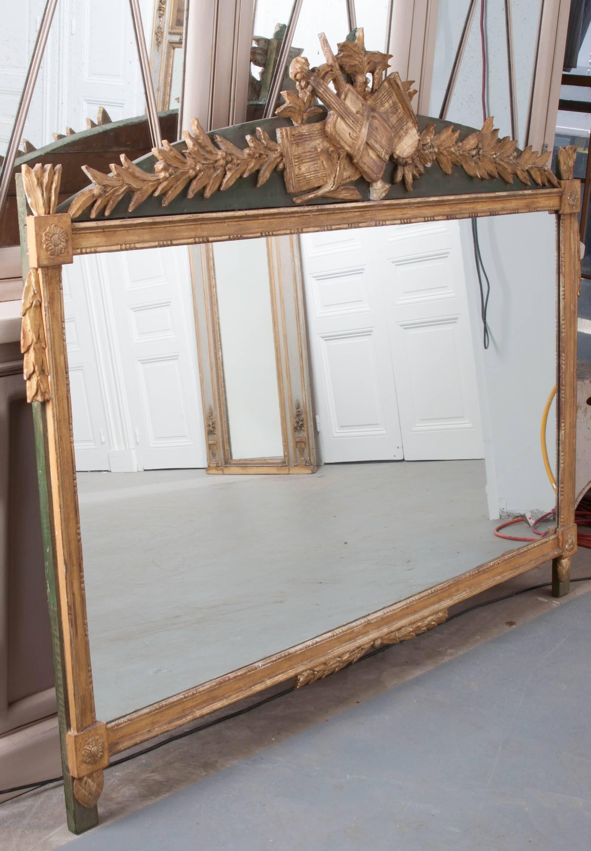 A fine French painted and gold gilt Empire mirror from 19th century France. The mirror’s back has been painted a deep hunter green that makes the brilliant gold gilt frame and crest stand out against the darker backing. The extraordinary crest is