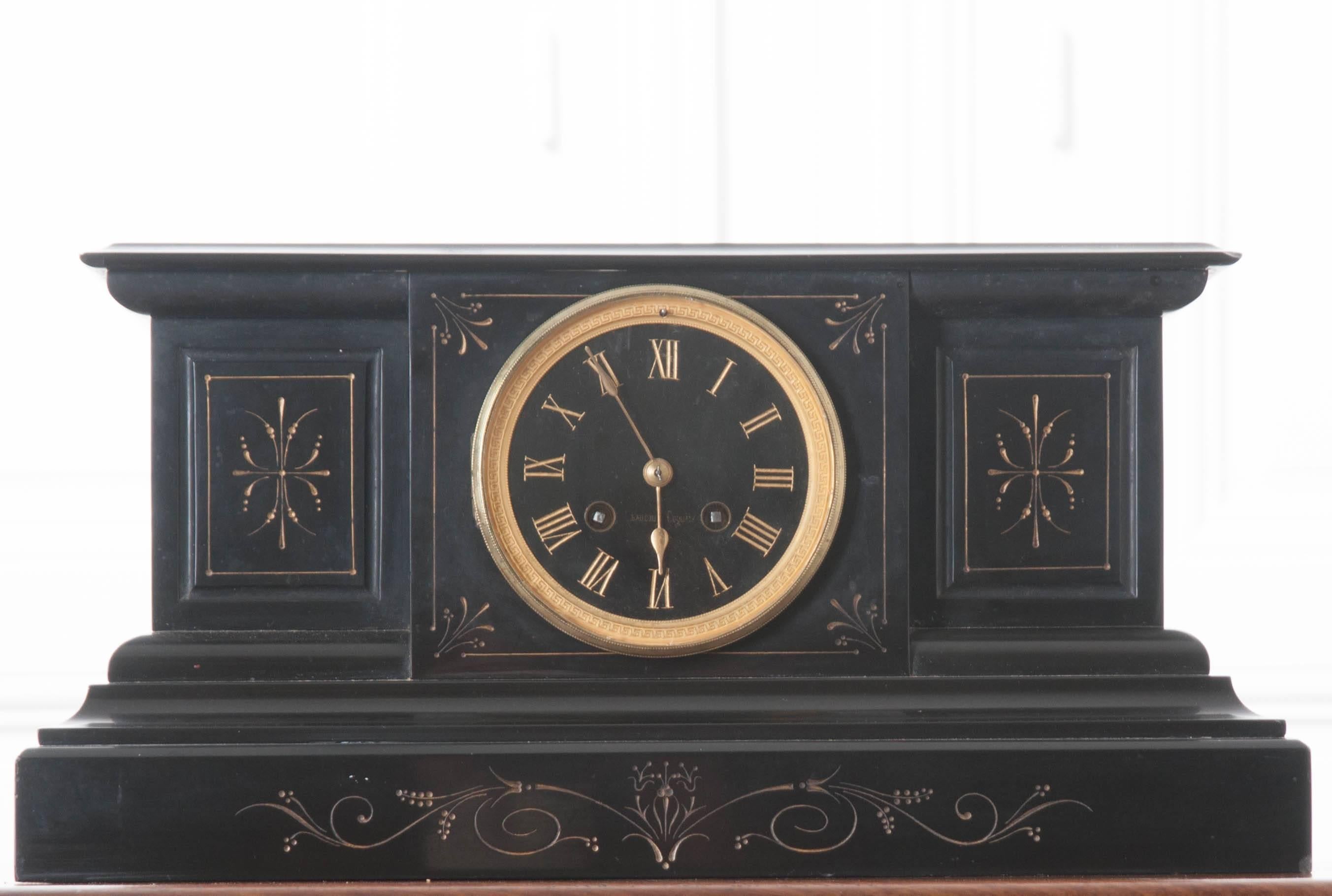 A striking ebony marble mantel clock with brass details from the turn of the 20th century, France. The clock’s body is made entirely of jet black marble, and decorated with scrolled and styled etchings that have been painted gold. The clock’s face