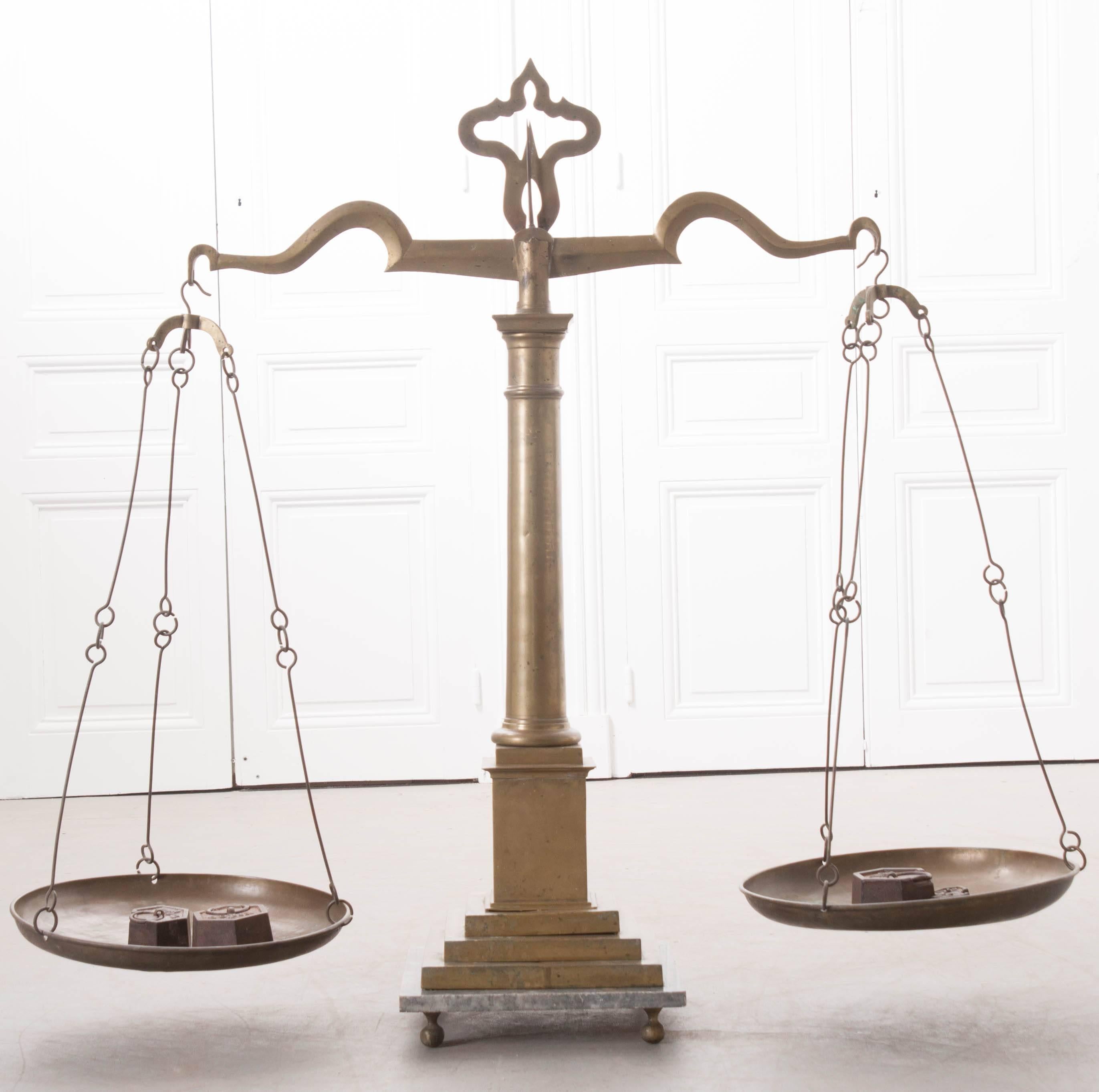 A stunning, large brass table scale, made near the turn of the century, England. The scale is no longer operational, but still makes an mighty impact on a space. The scale is made of brass, with two copper weigh pans. The shaped arms support the