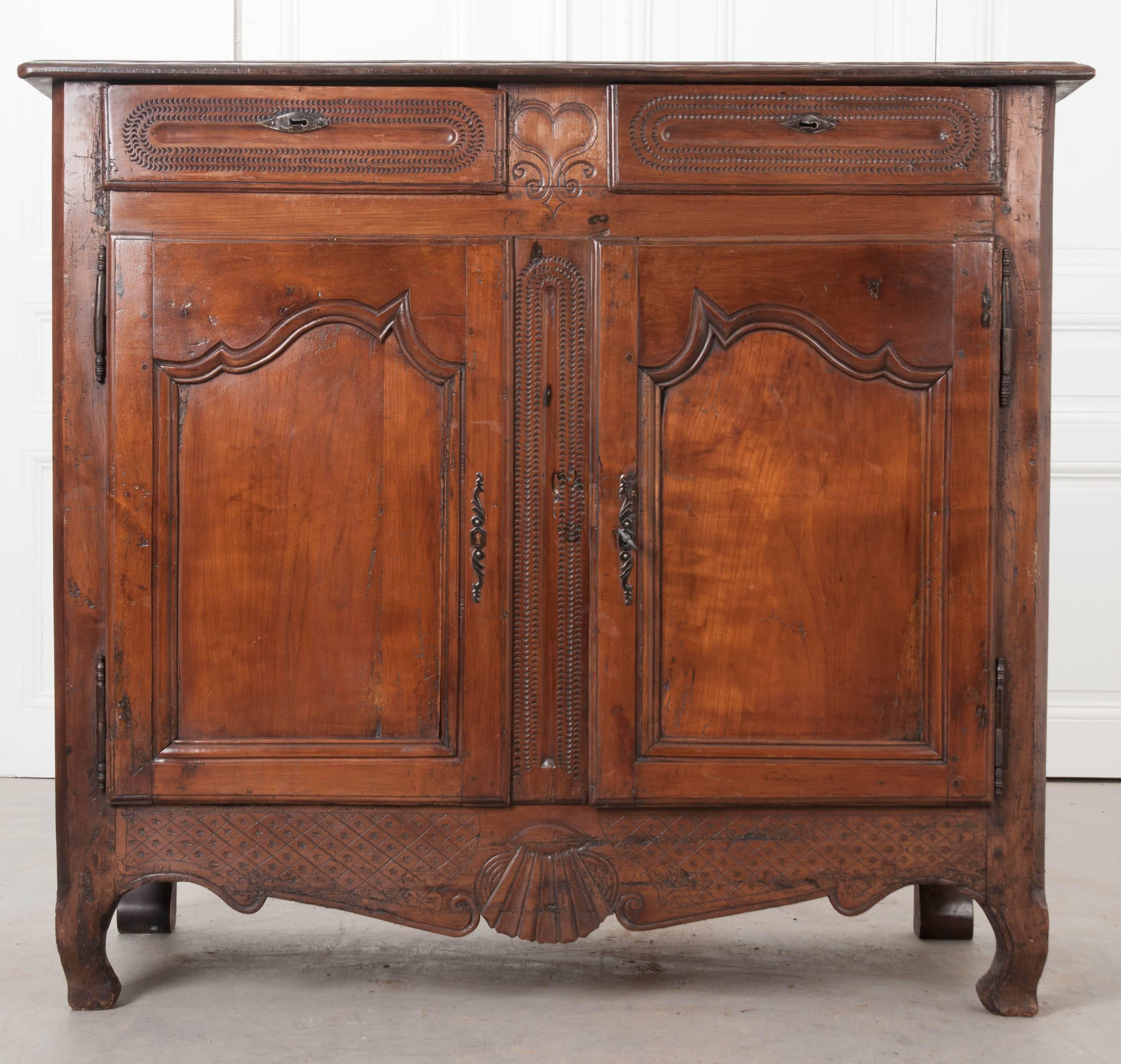 A charming, hand-carved cherry buffet from the late part of the 18th century. This remarkable antique features wonderfully carved details on nearly every surface. The two drawers that can be found in the apron are decorated with a continuous half