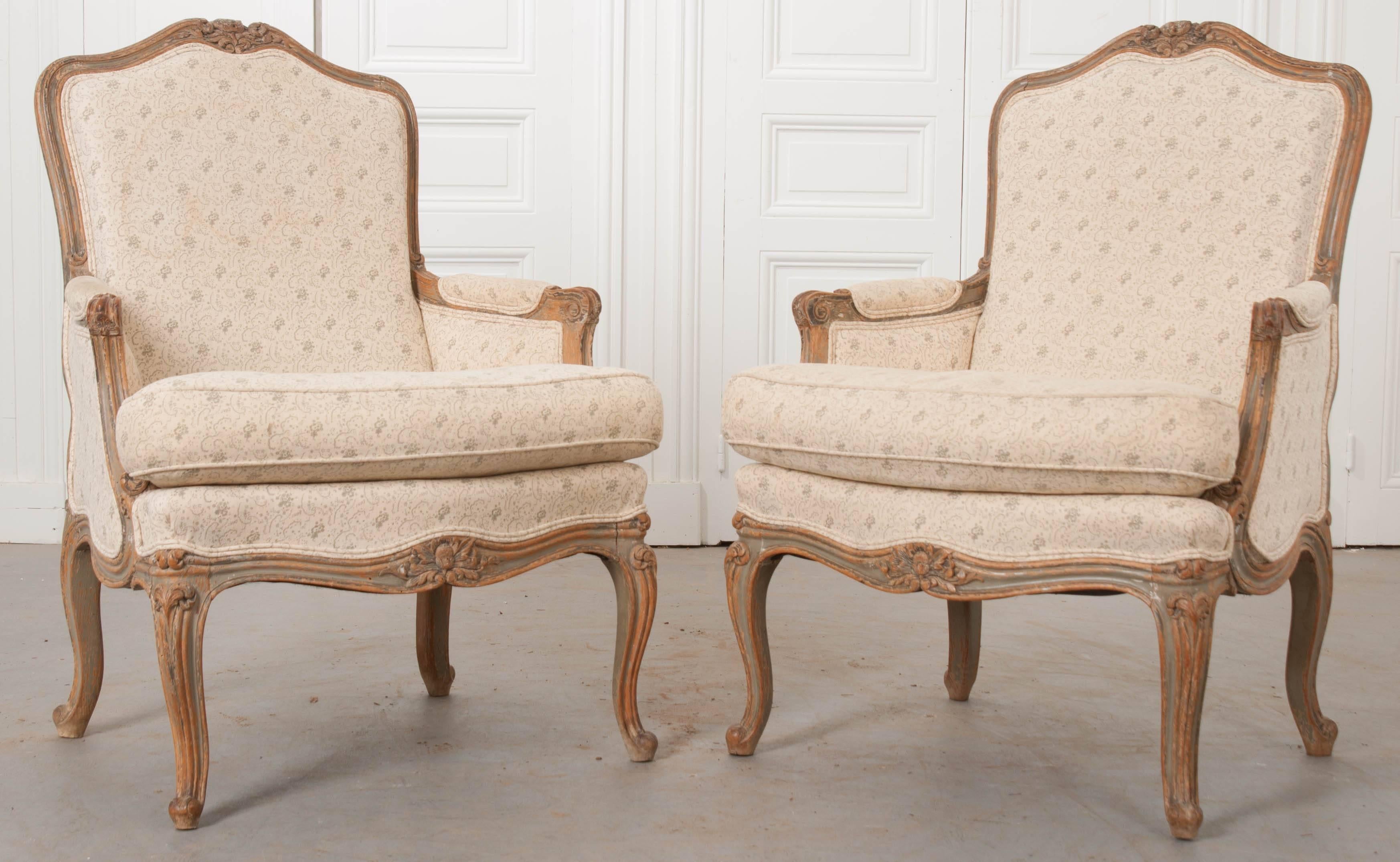 A fabulous pair of carved and painted Louis XV style bergères from 19th century France. These beautiful chairs are upholstered in a patterned linen and have a soft green plaid upholstered posterior. The upholstery is not original to the pair, and