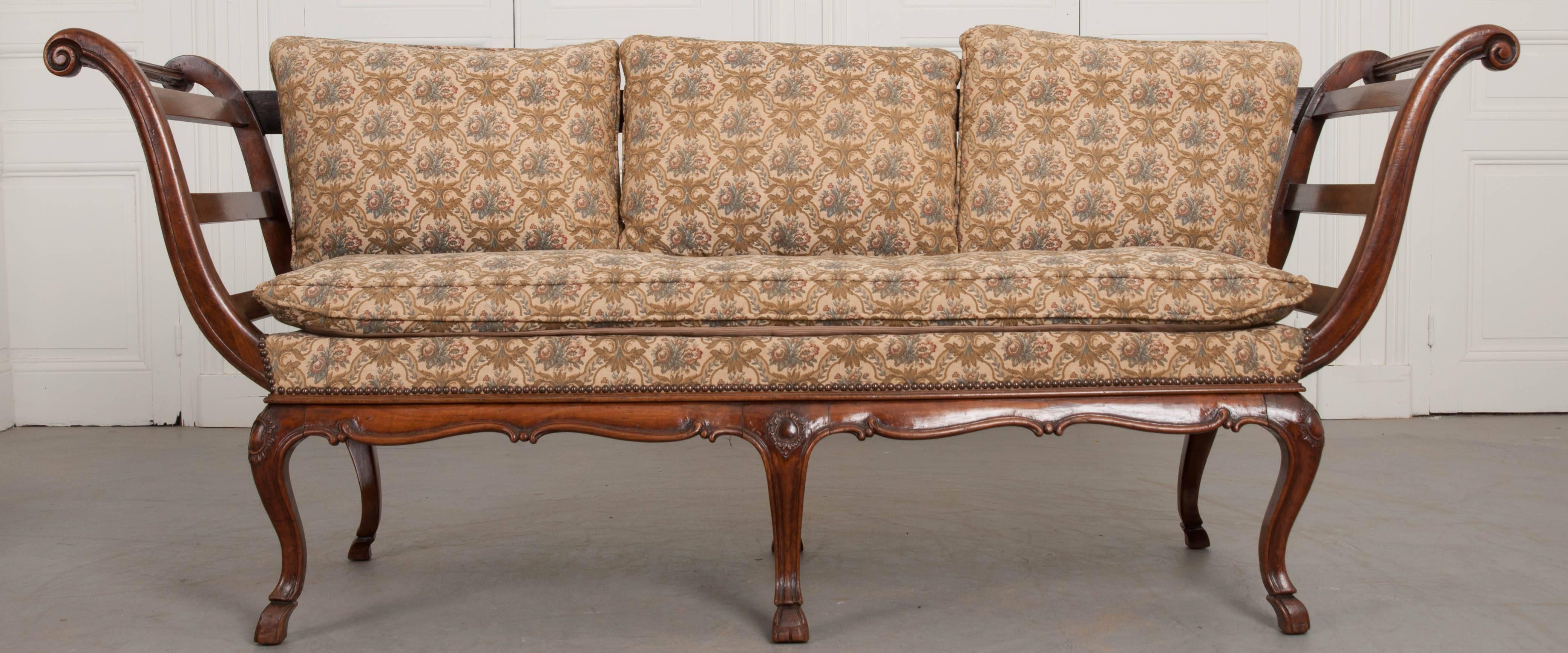 An outstanding Louis XV style settee, totally hand-carved in walnut, from the 18th century, Italy. The upholstered settee has fantastic, scrolled arms that instantly grab your attention. The sides and back of the sofa are open, with carved walnut