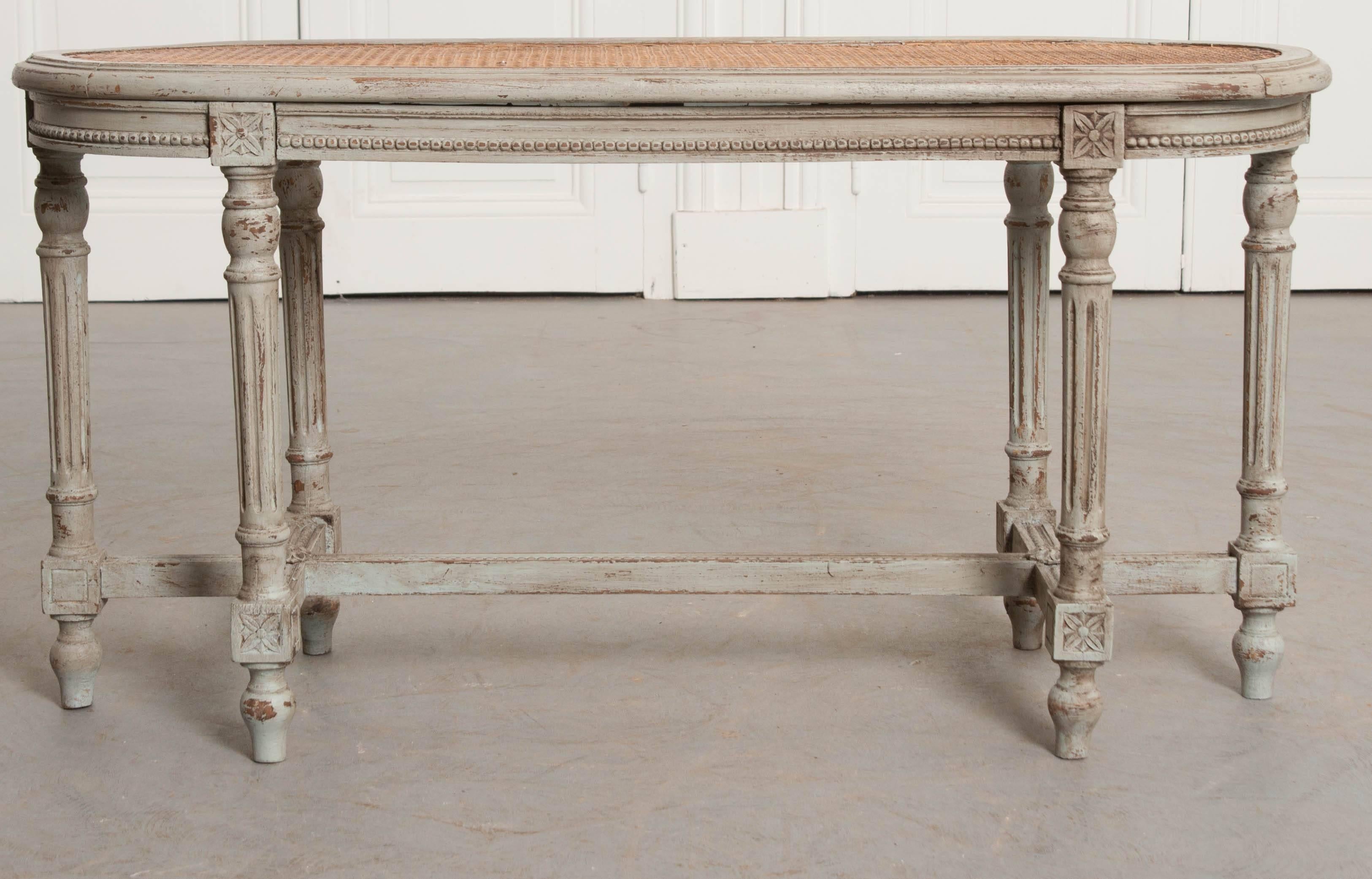 A lovely caned bench, done in the Louis XVI style, from 19th century France. This wonderful antique bench has been recently painted a French gray color that has undergone a process to give the new finish the appearance of age. The woven cane seat is