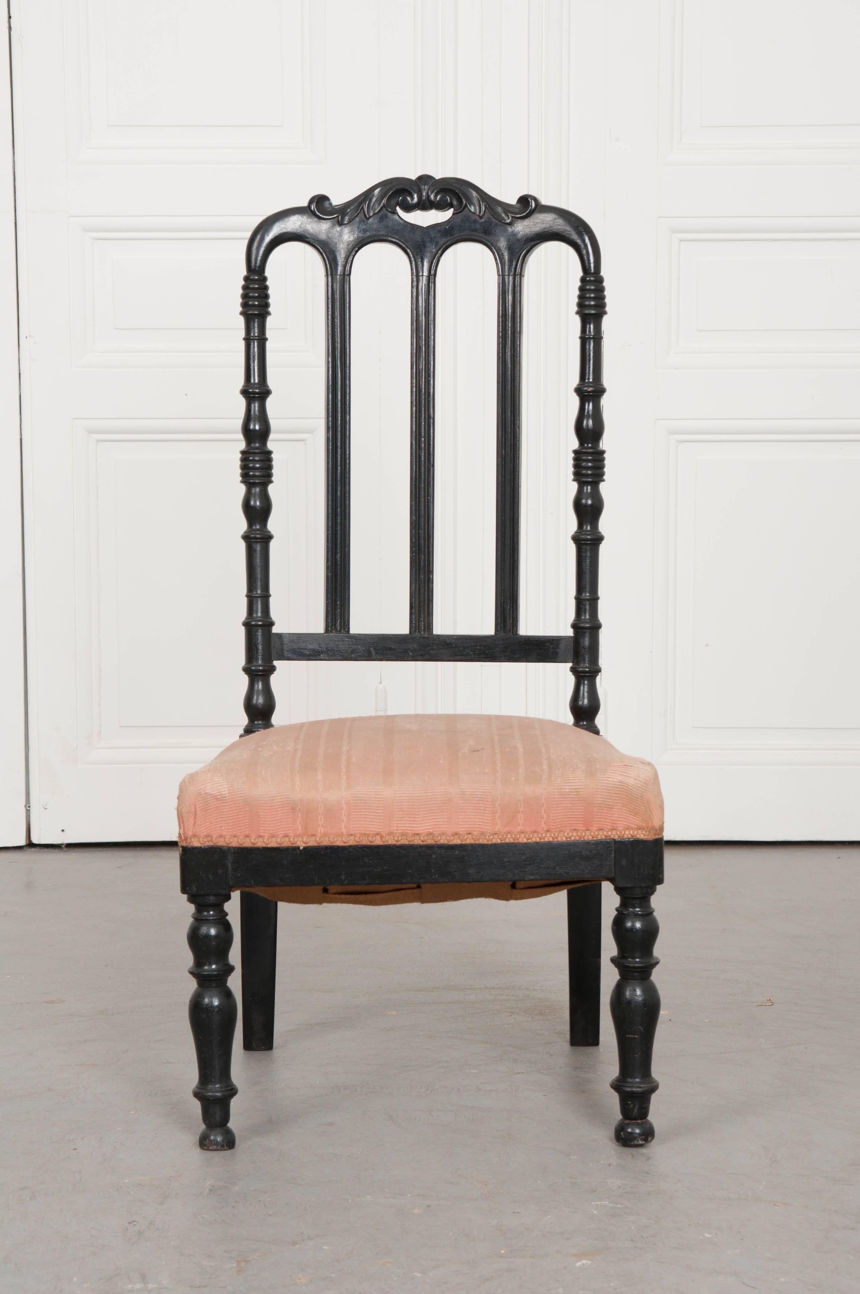 A precious ebony slipper chair from 19th century France. The ebony chair has an ornately carved crest rail that is pierced. The stiles are brilliantly turned and have ribbed motifs. The three centre splats are linear with restrained carvings. The