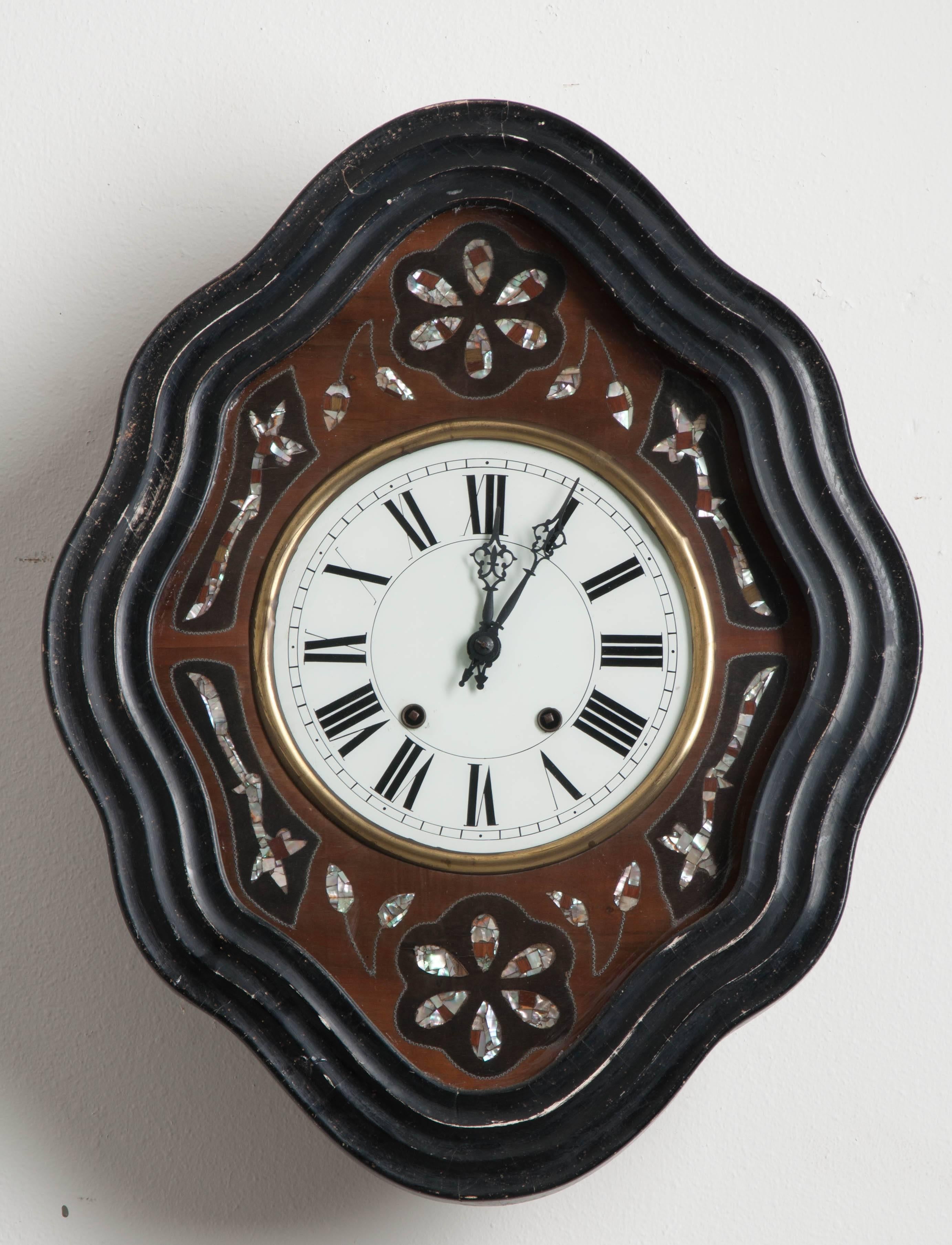 Diese Uhr aus dem 19. Jahrhundert besticht durch ihren rautenförmigen, gewellten Uhrenrahmen aus ebenholzfarbenem Holz. Blumen- und Blattmuster aus Perlmutt sind in unterschiedlich gebeiztem Mahagoni und glänzendem Perlmutt eingelegt und umgeben das