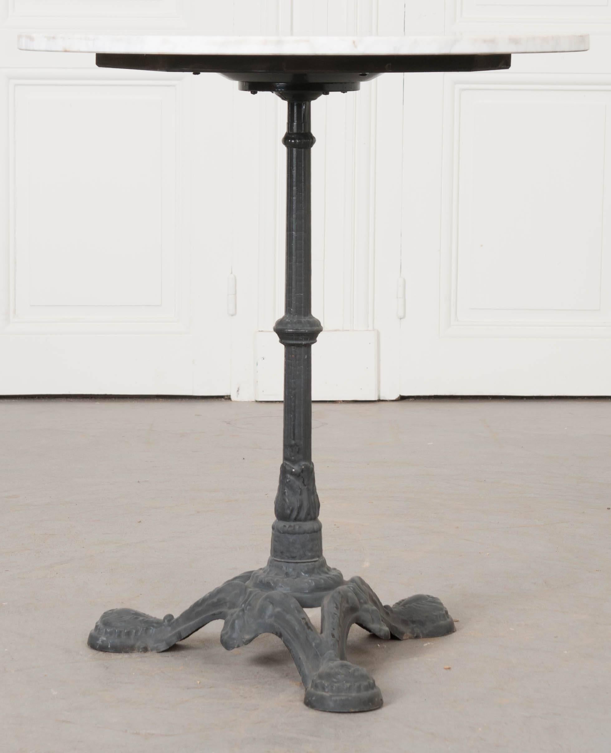 A classically styled French bistro table, with iron base and marble top, from the early part of the 20th century. The black painted base is made of cast iron, with three feet, and details in twisted ribbon and scrolled leaf motifs. The circular