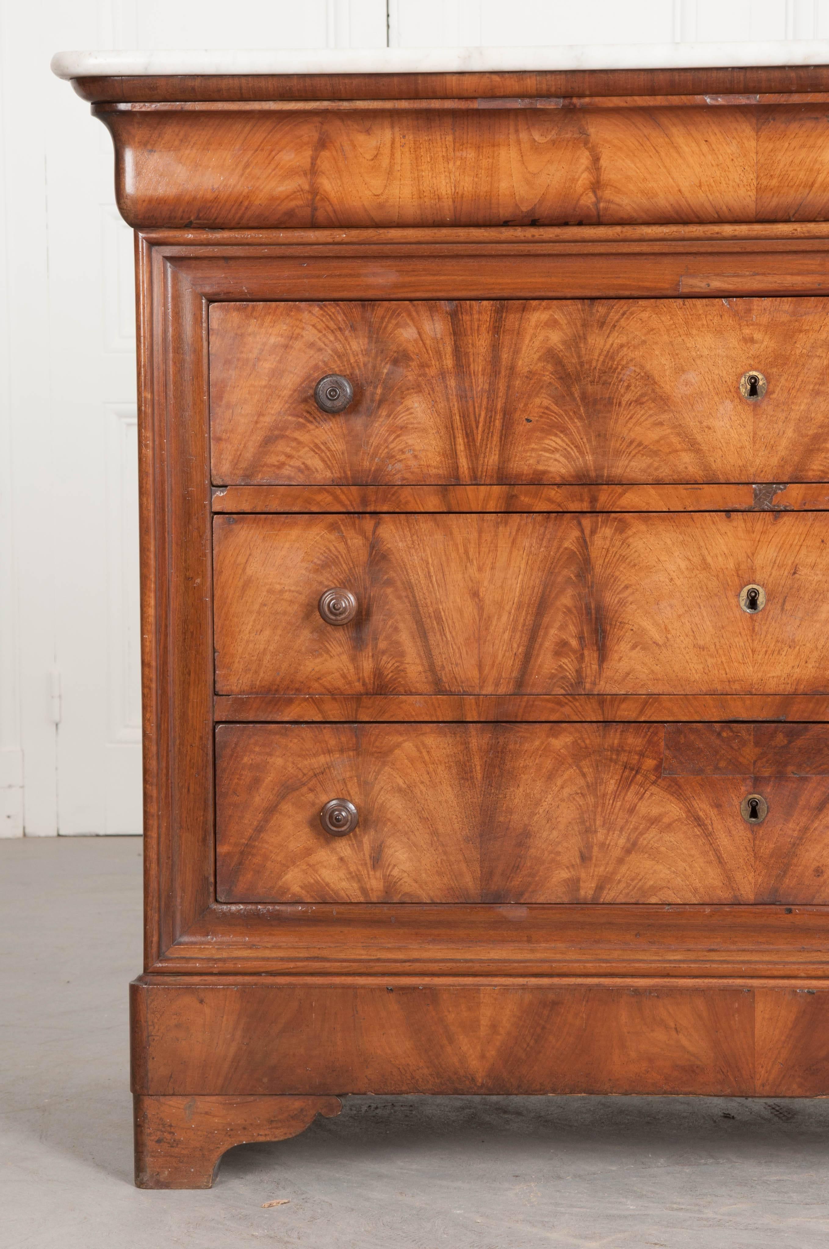 A fantastic mahogany Louis Philippe four-drawer commode from 19th century France. The commode is topped with a beautiful piece of antique marble, with rounded front corners that fit the body perfectly. The shaped apron is, in fact, a hidden drawer.