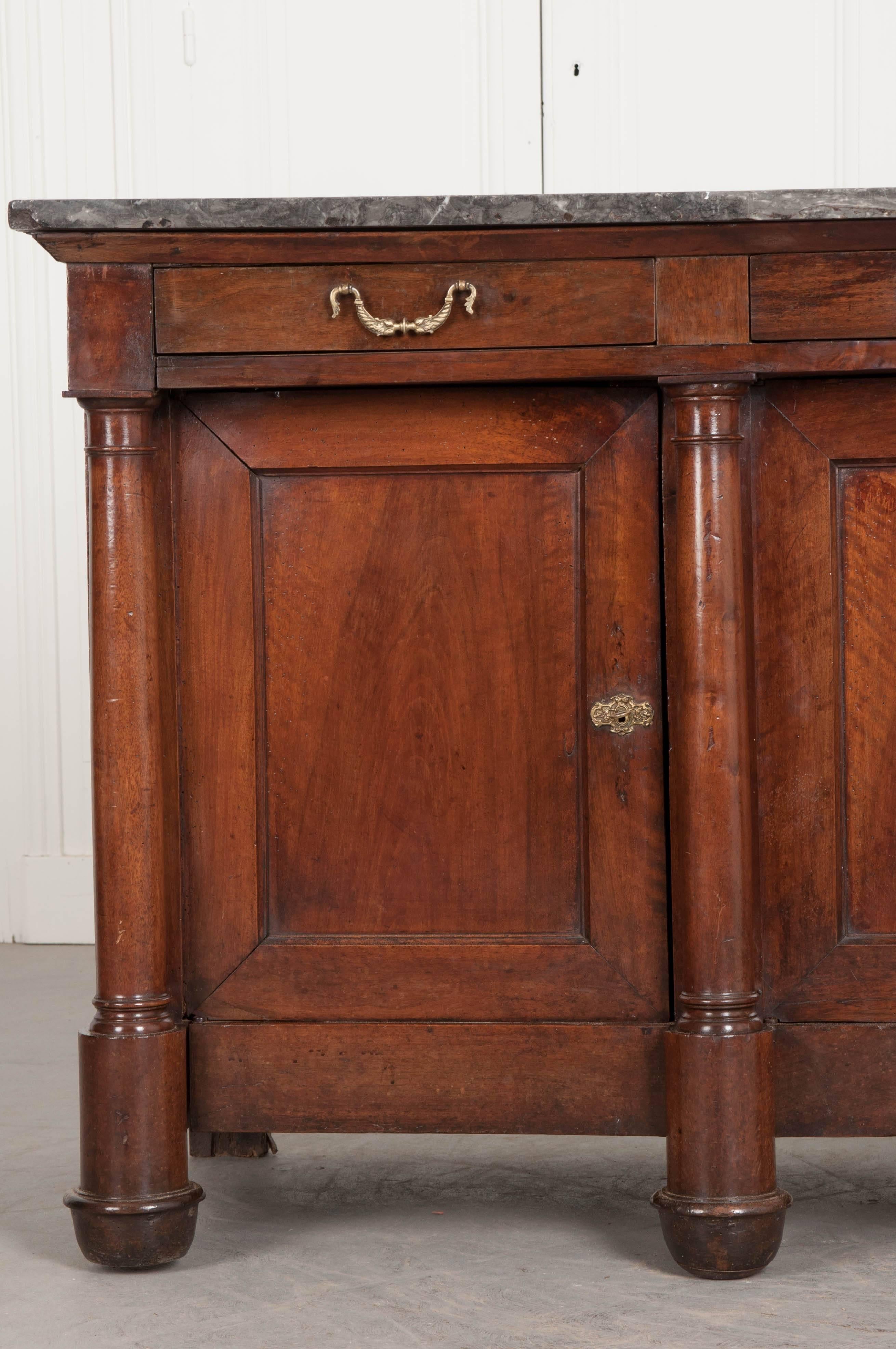 This striking mahogany enfilade, done in the Empire style, was made in France, circa 1860. The marble top is gray, with some flashes of pink, and has been repaired in its lifetime. It rests nicely atop an extraordinary mahogany enfilade, featuring