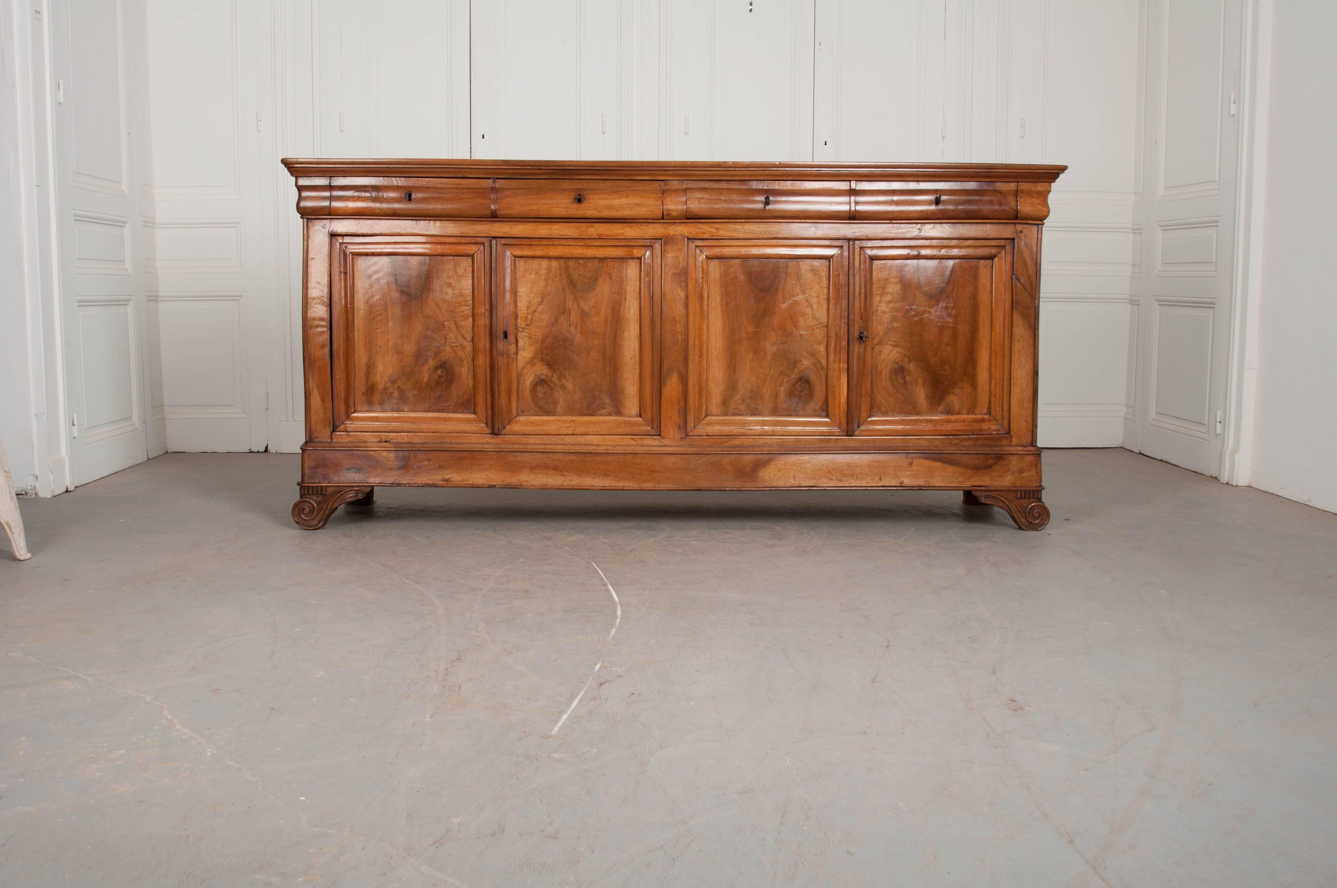 A remarkable solid walnut four-door Louis Philippe enfilade, from 19th century France. The antique case piece has four lockable drawers that are situated about its four lockable doors. This enfilade boasts incredibly beautiful walnut, with