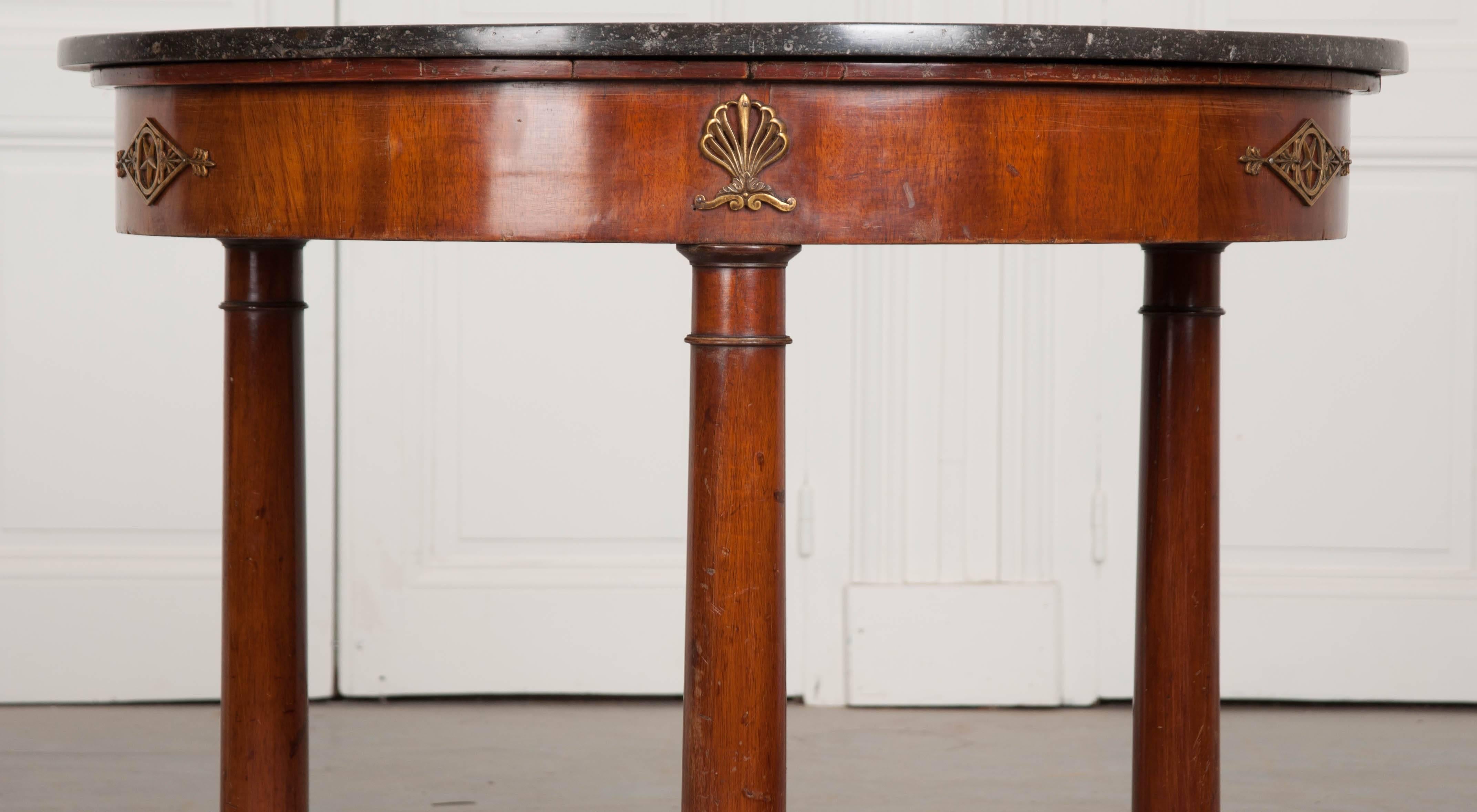 A handsome mahogany centre table, in the Empire style, from 19th century, France. The circular table is topped with a fabulous piece of black fossil marble, filled with tiny ancient sea creatures that have become set in stone. The apron is decorated