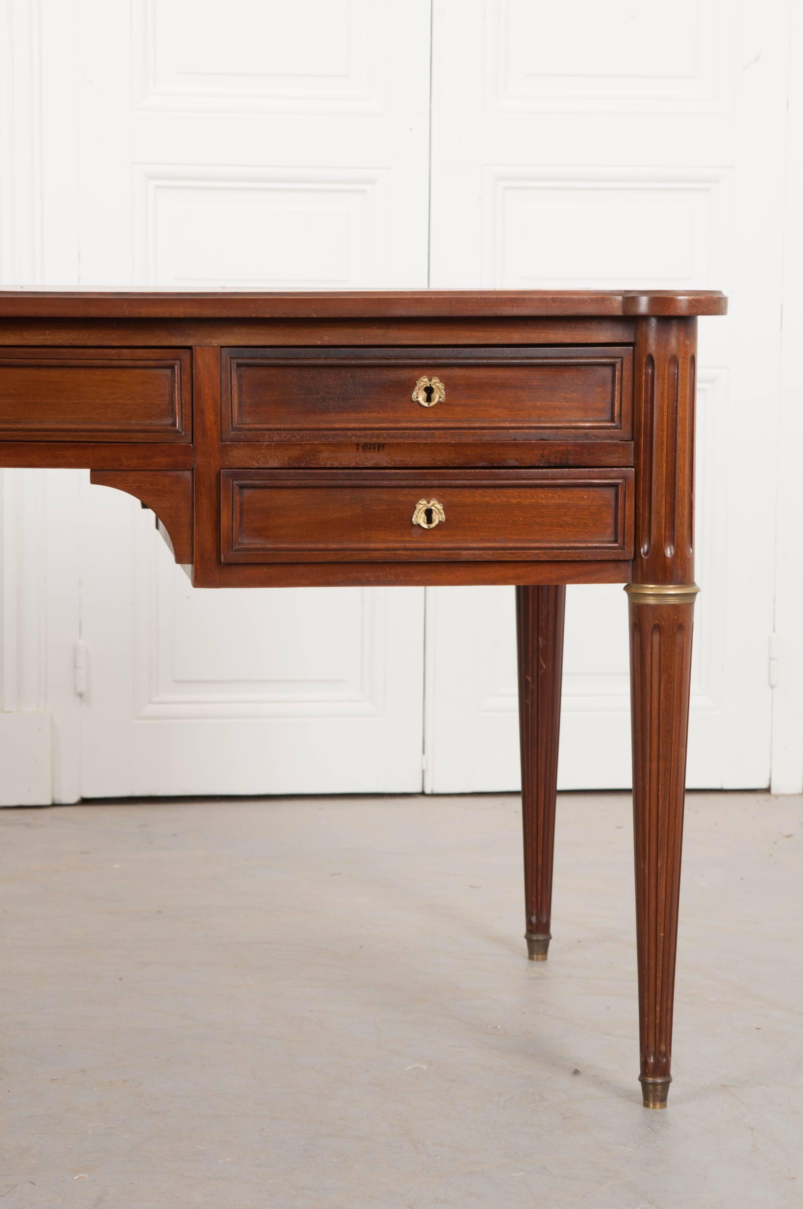 A remarkable mahogany Louis XVI style desk from France. The desk’s top has been clad in an outstanding cognac colored leather that has been embellished with gold tooling that can also be found on the slides that extend from each end of the desk. The