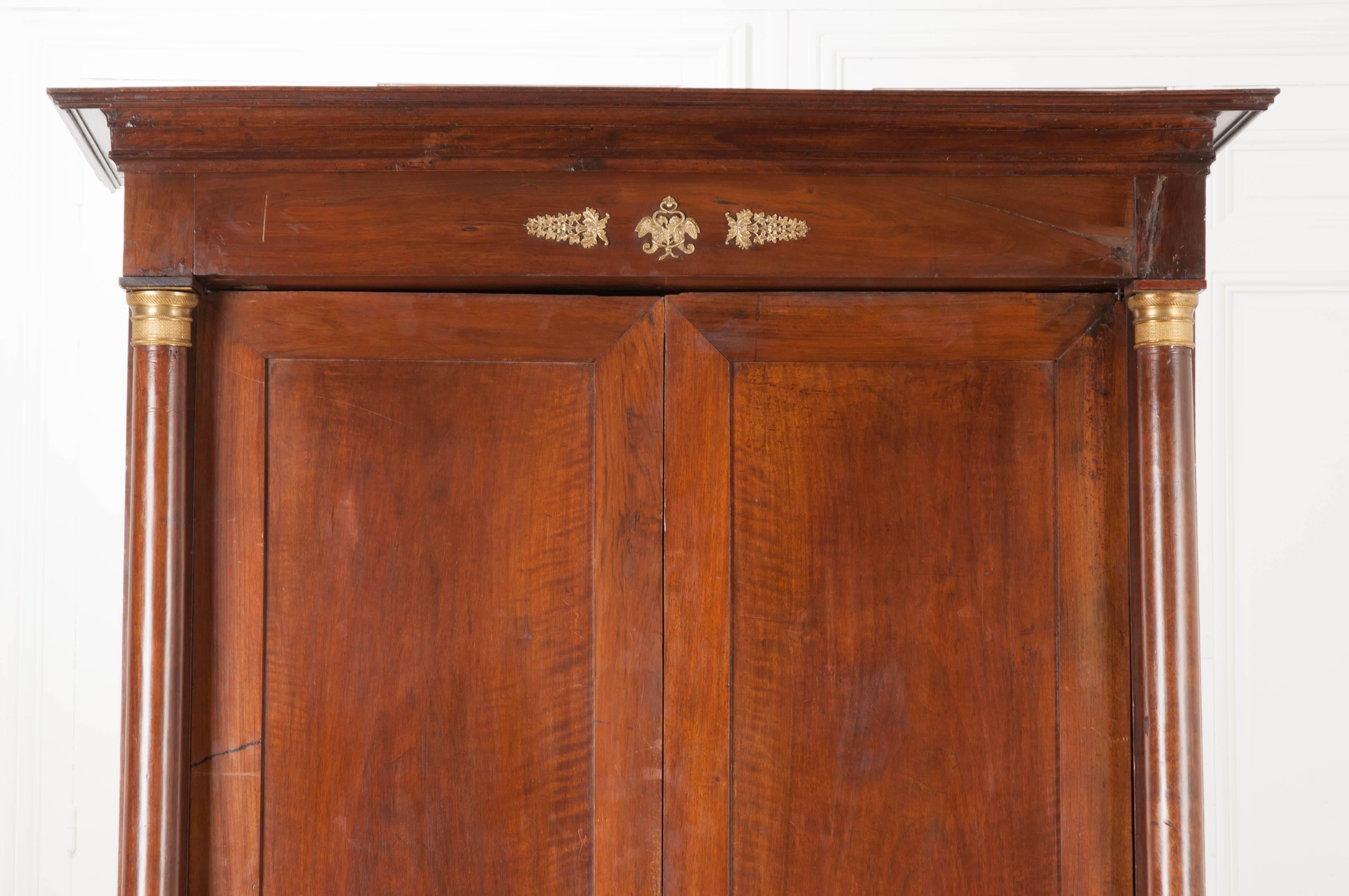 A striking walnut Empire period armoire from France. Two freshly waxed doors are flanked by walnut columns that have both brass capitals and brass bases. Near the cornice, brass ormolu in the image of eagles, serpents, foliage and trees can be found