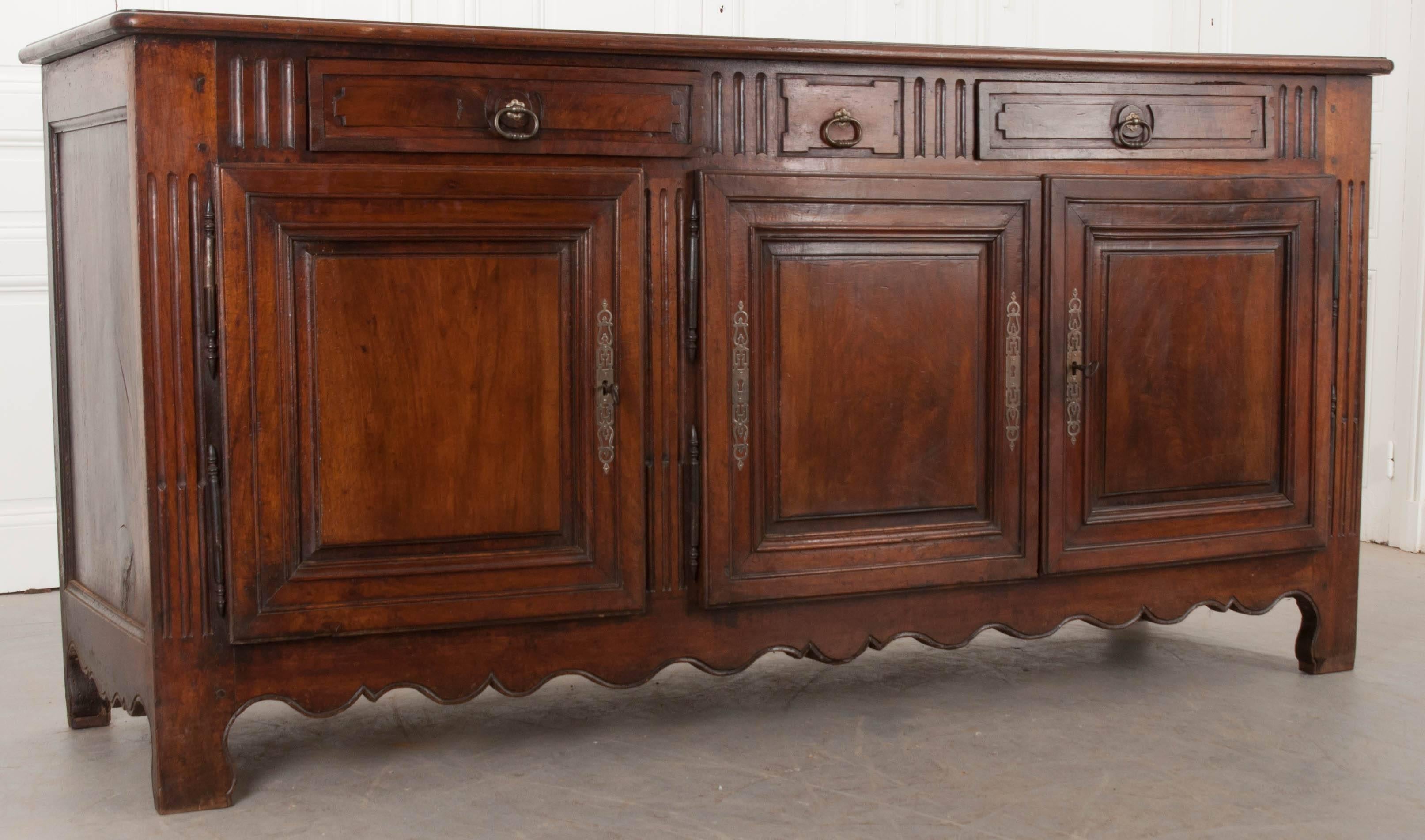 A grand solid-walnut enfilade from 19th century Provincial France. This large case piece has three hand-carved panel doors, with working locks, that are hung on steel barrel hinges dominating the façade. Above these doors are two drawers, equipped