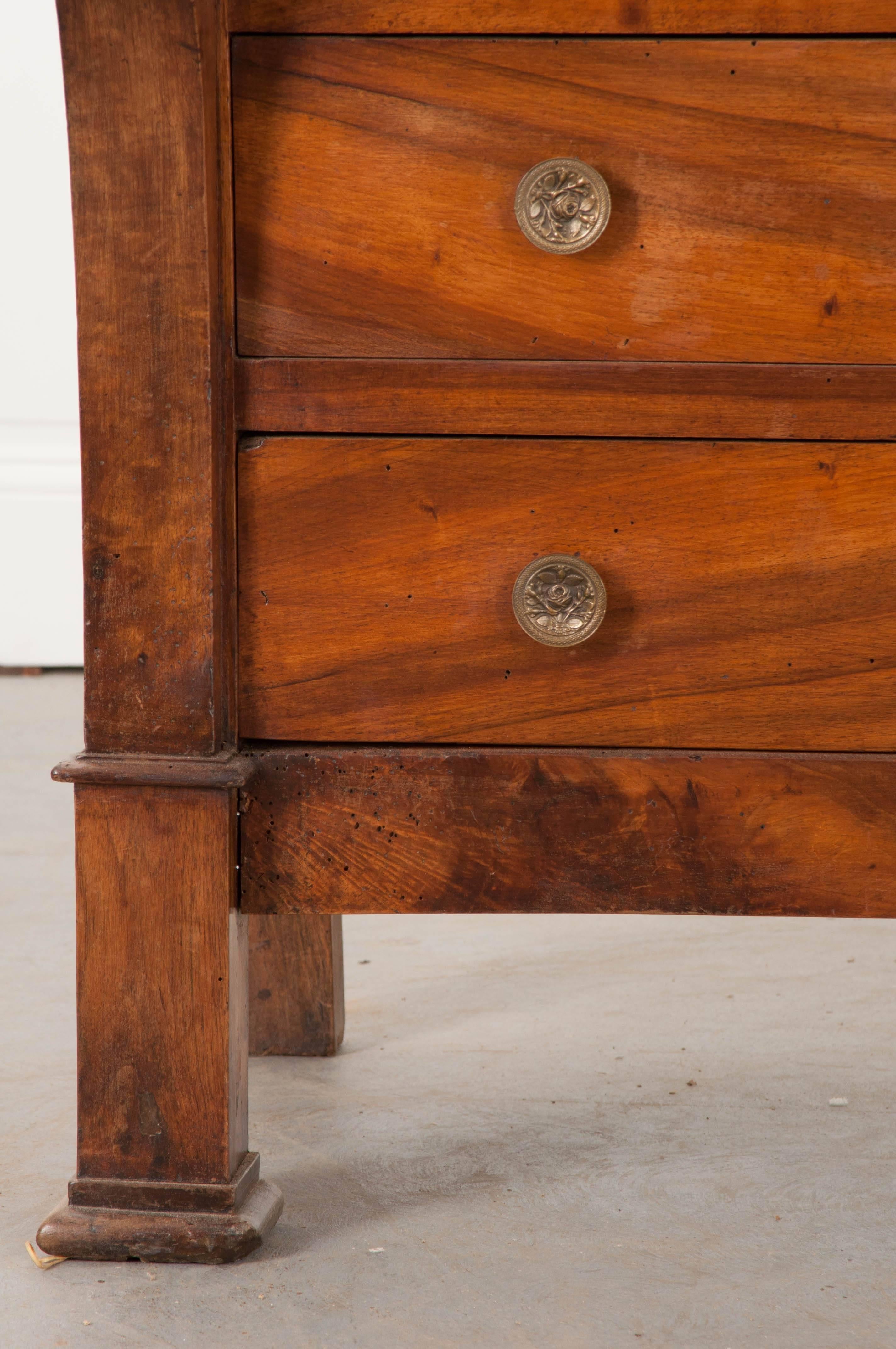A spectacular four-drawer walnut commode, done in a transitional style, from 19th century France. The chest incorporates elements from the French Empire and Restauration styles. The topmost drawer is hidden in the apron. The lower three each have