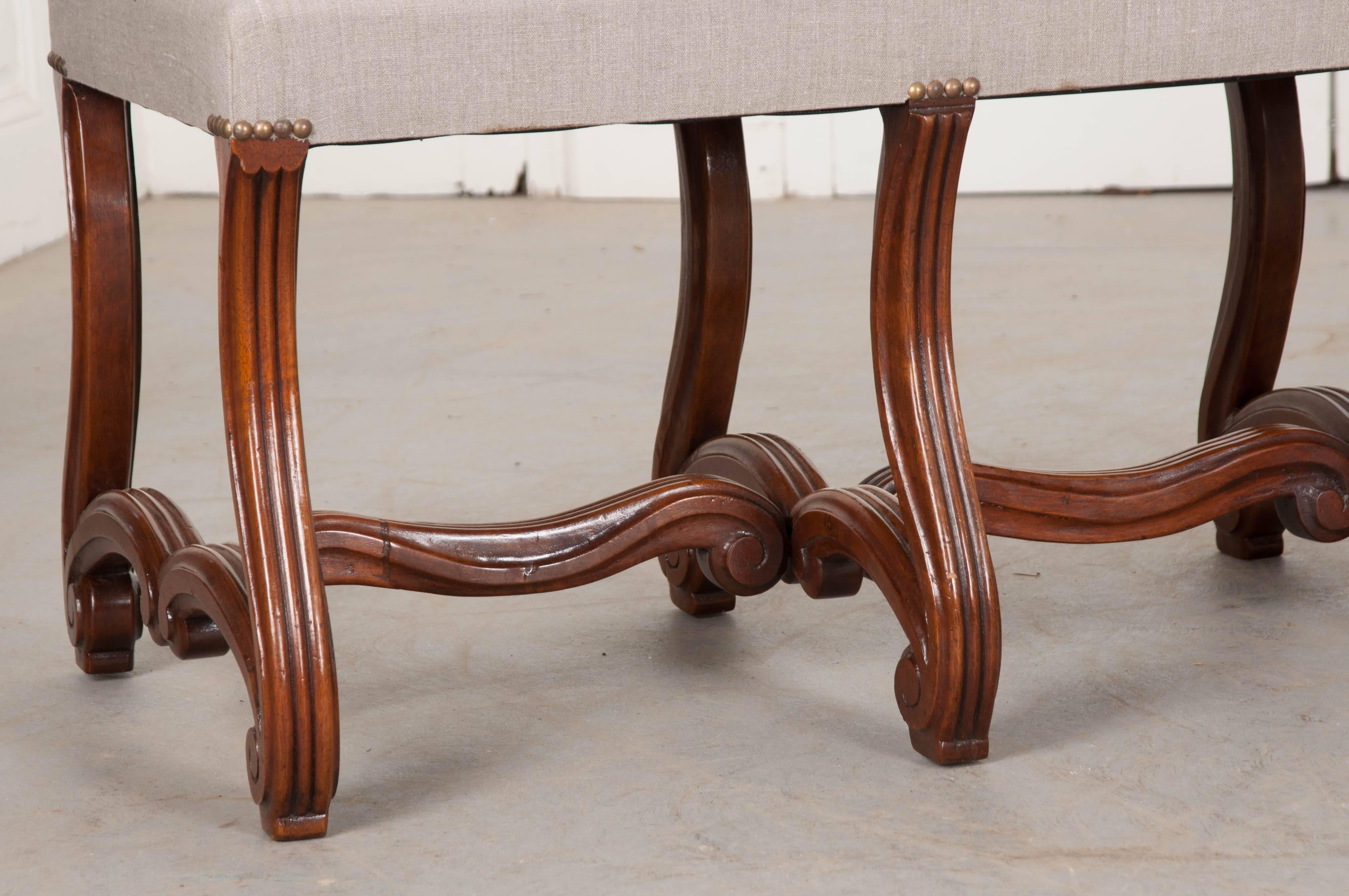 A fine pair of French 19th century Louis XIV style mahogany benches, upholstered in a taupe or grey linen that is affixed to the base with antiqued brass nail heads at each leg. The exceptionally well-carved bases give this pair their exceptional