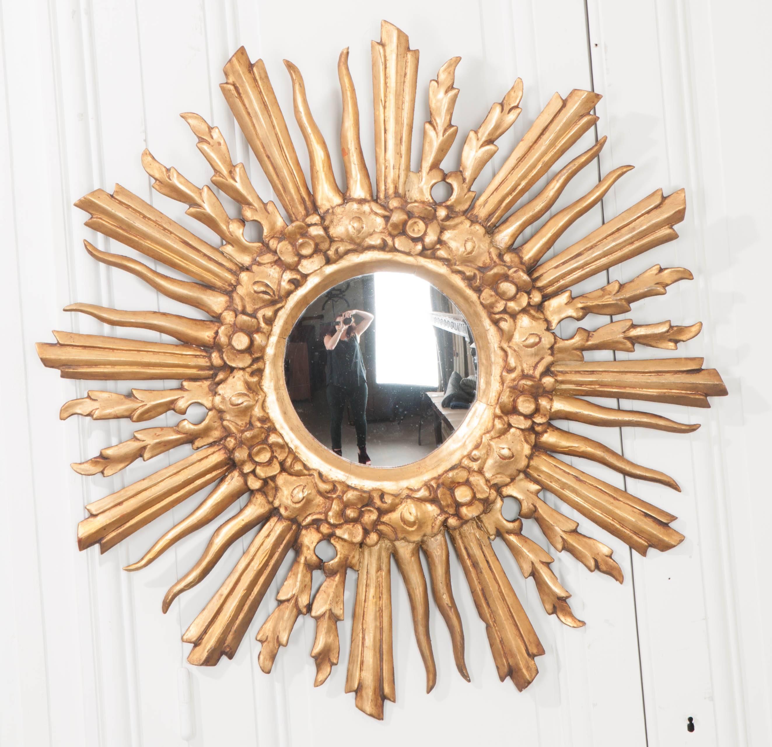 A brilliant French starbust mirror, with spectacular gold gilt, from the 19th century. The smaller central convex mirror is original to the antique and surrounded by beautifully carved flowers that are arranged in a wreath around the glass. From