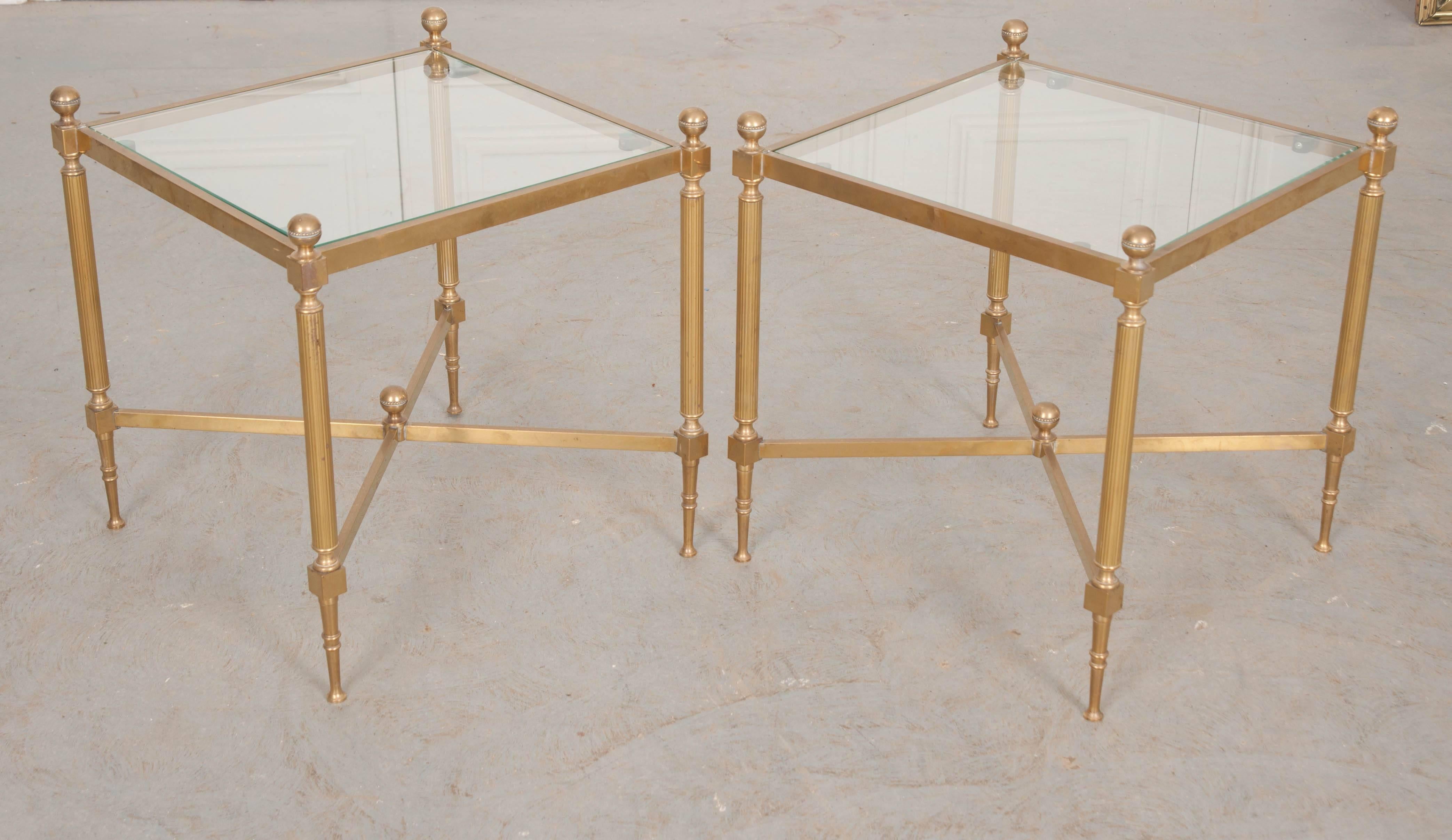 A sharp pair of early 20th Jansen style square side tables, made of brass and glass in the early 1900s, France. The tables have radiant brass frames with an inset glass top. The tables’ legs are pushed to the corners and decorated with reeded shafts