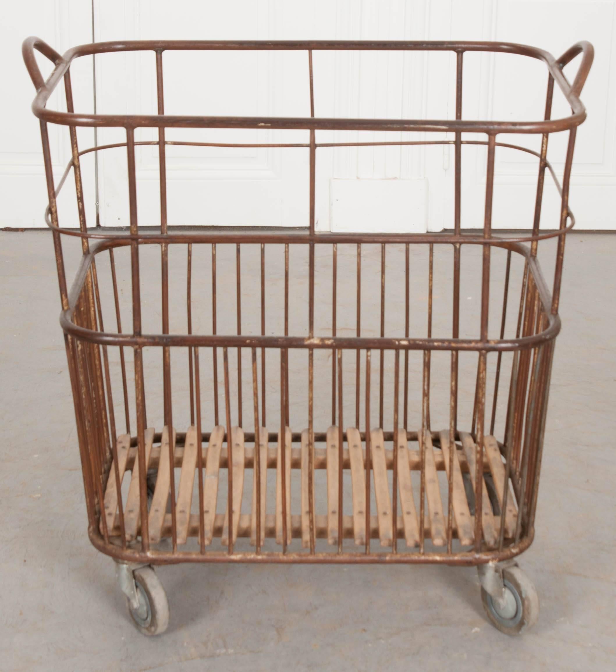 An excellent French bakery or baguette basket from the early part of the 20th century, France. The tall metal basket has two handles and rolls on large caster wheels for easy movement. The bottom is made of wooden slats that have been slowly