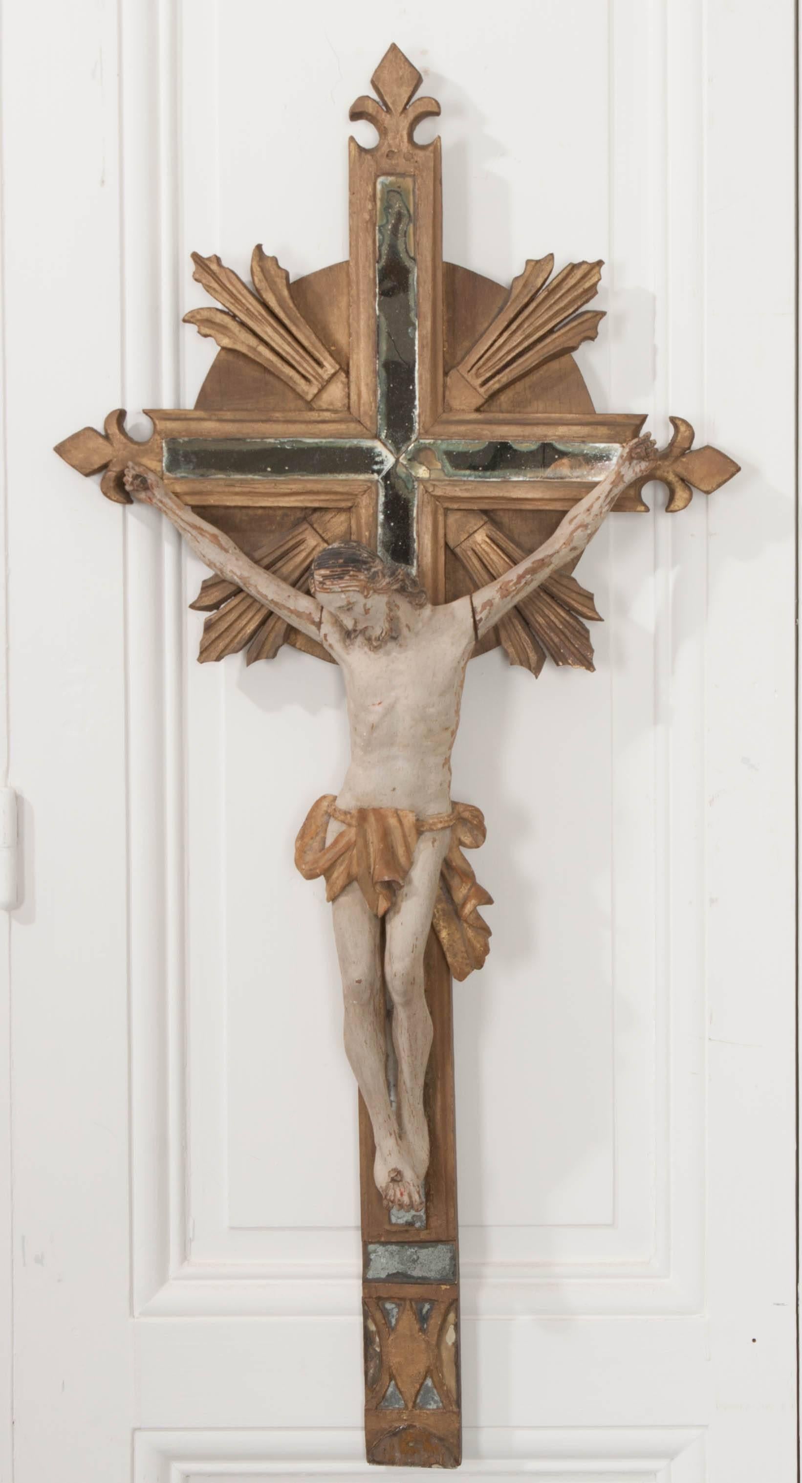 A remarkable hand-carved crucifix from 19th century France. This extraordinary religious artifact has been finished in a beautiful gold gilt and was made with antique mercury glass set into the cross. This glass is impeccably well-aged and adds to