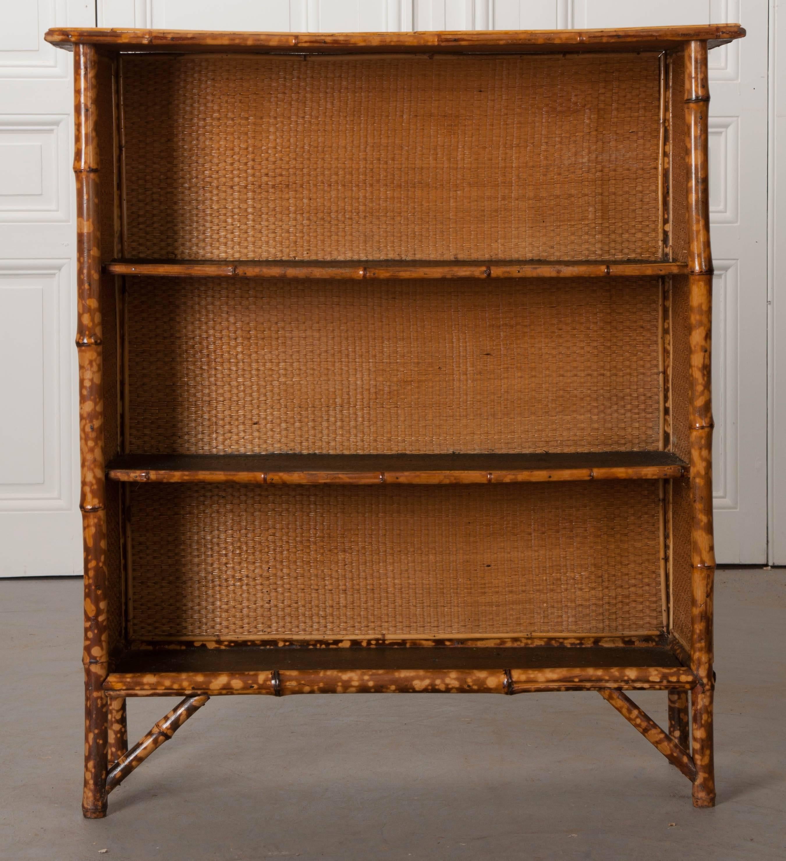 A wonderful English bamboo bookshelf from the 1890s, that has been recently refinished. It has been finished in a gorgeous black and gold découpage. The woven seagrass found in the interior is remarkably intact. This small bookcase has two center