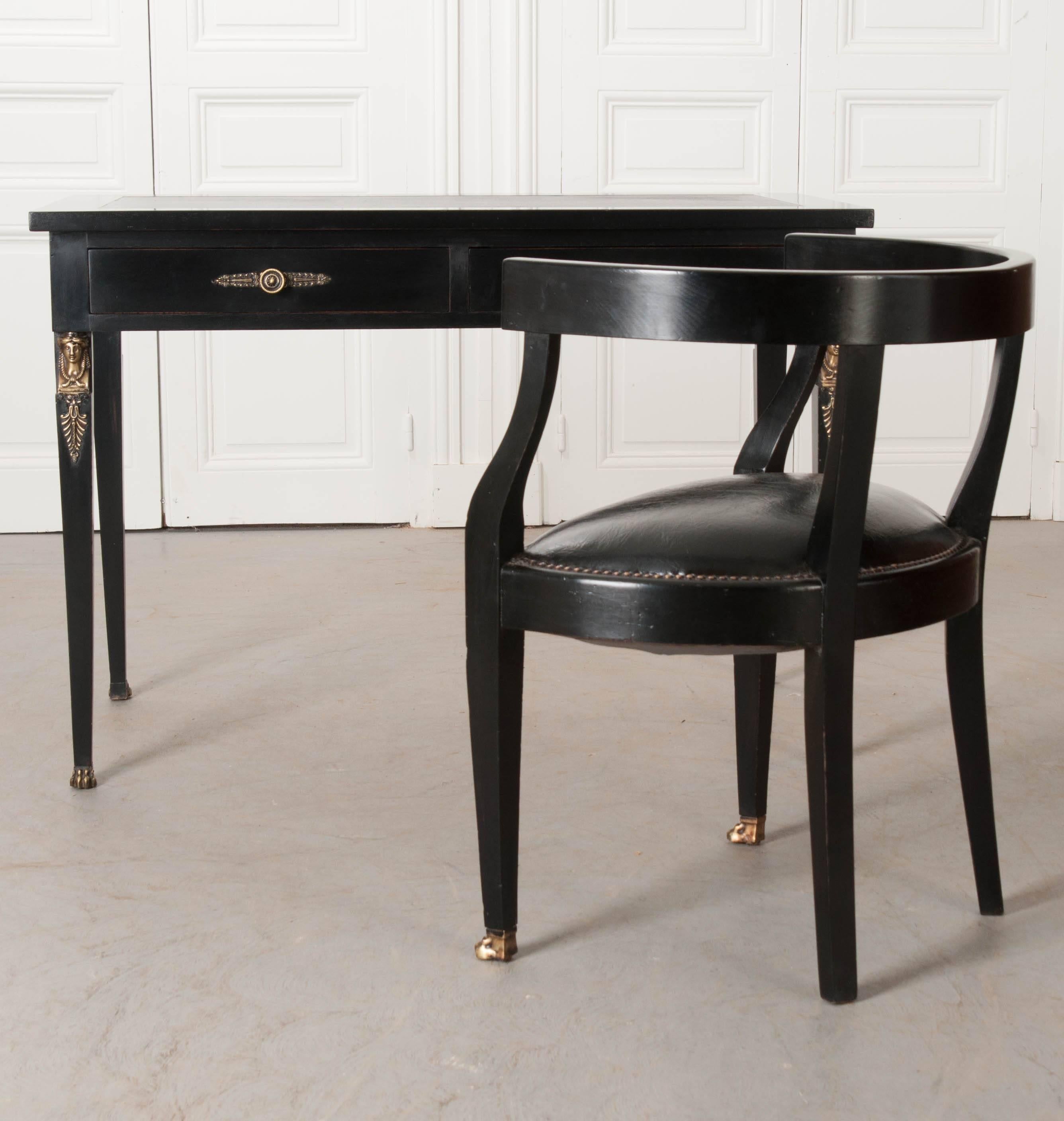 An incredibly handsome ebonized desk and chair, in the Napoleon III style, from 1920's France. Both the chair and desk are topped in black leather, with brass nail heads securing the chair’s leather seat to its frame. Each piece of the ebony set are