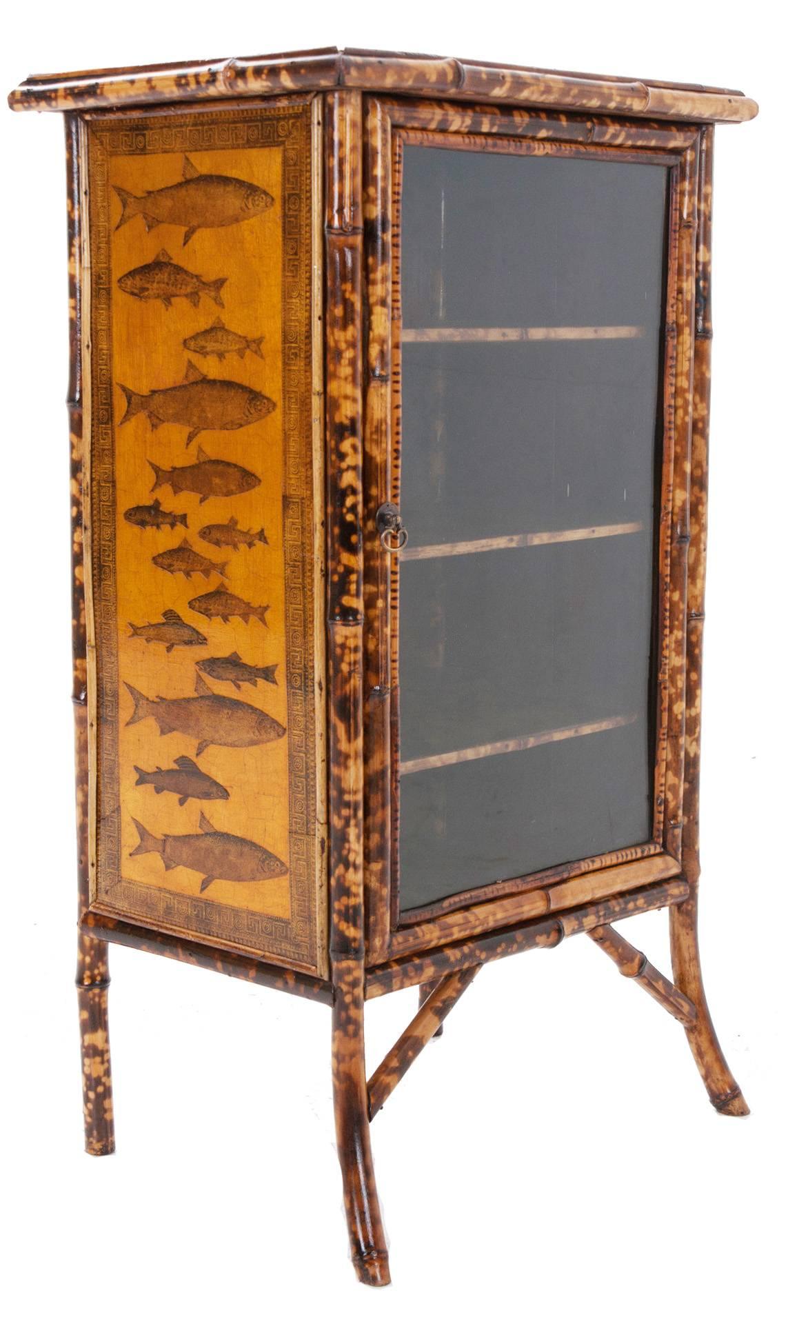 English, 1890s bamboo cabinet is sturdy and re-finished with black and metallic yellow paint overlaid with decoupage of fish and an interesting boarder, one framed glass door with three original twail shelves.