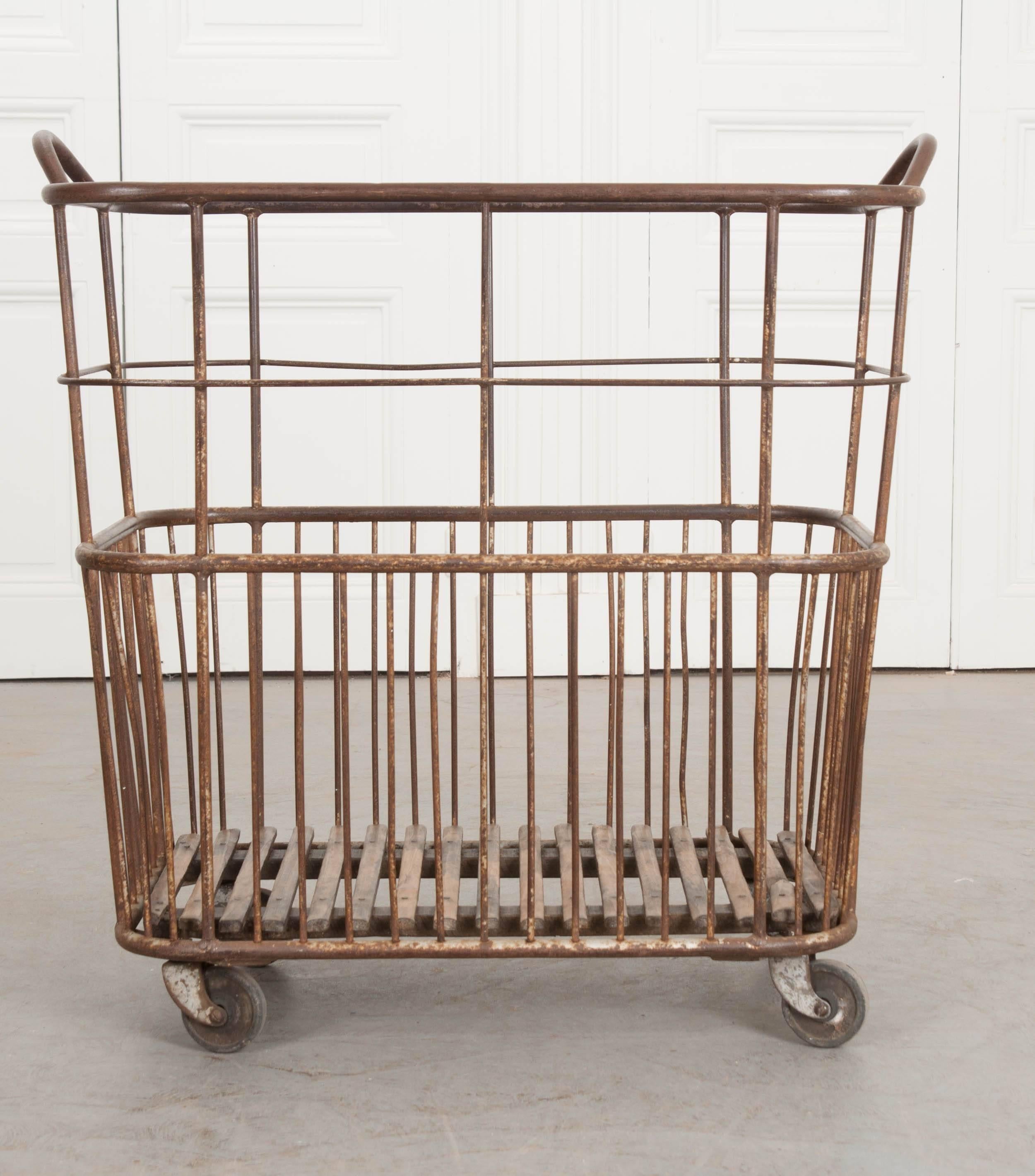A delightful French bakery or baguette basket from the early part of the 20th century, France. The tall metal basket has two handles and rolls on caster wheels for easy movement. The bottom is made of wooden slats that have been slowly patinated