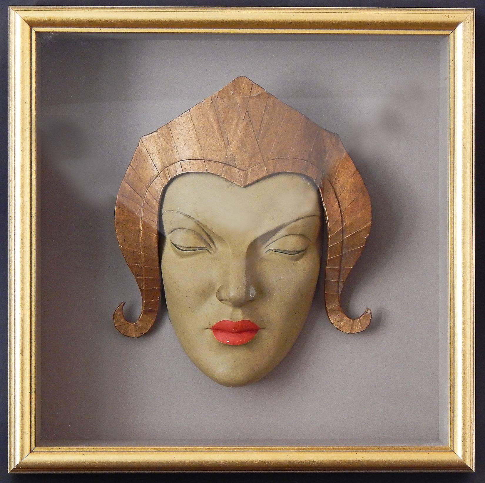 Stunning and exotic, this pair of Art Deco masks, framed in deep shadow boxes, are beautifully sculpted and painted, each with gilded South Asian headdresses that hint at high fashion and Hollywood spectacles. They make a spectacular pair, and