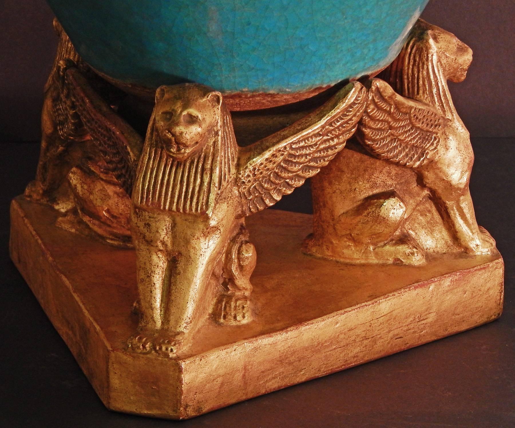 Fabulous and rare, this large, stunning Egyptian Revival bowl resting on a gold-glazed base with three winged lion figures was made in 1919 by Leon Volkmar in Bedford Village, New York. The brilliant blue glaze of the bowl -- which borrows from