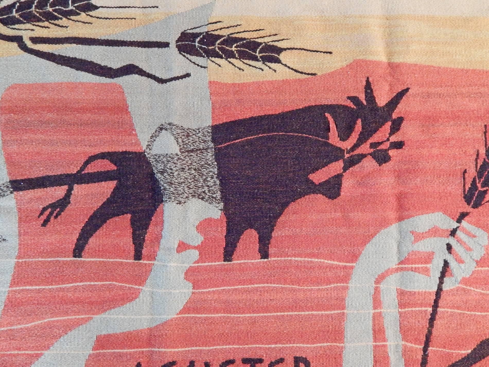 Woven from gorgeous yarns in coral, wheat, pale slate and black, this stunning Mid-Century tapestry depicts two layered images -- a classical figure holding a stalk of wheat, superimposed over a plowman with two bulls. Clearly showing the influence