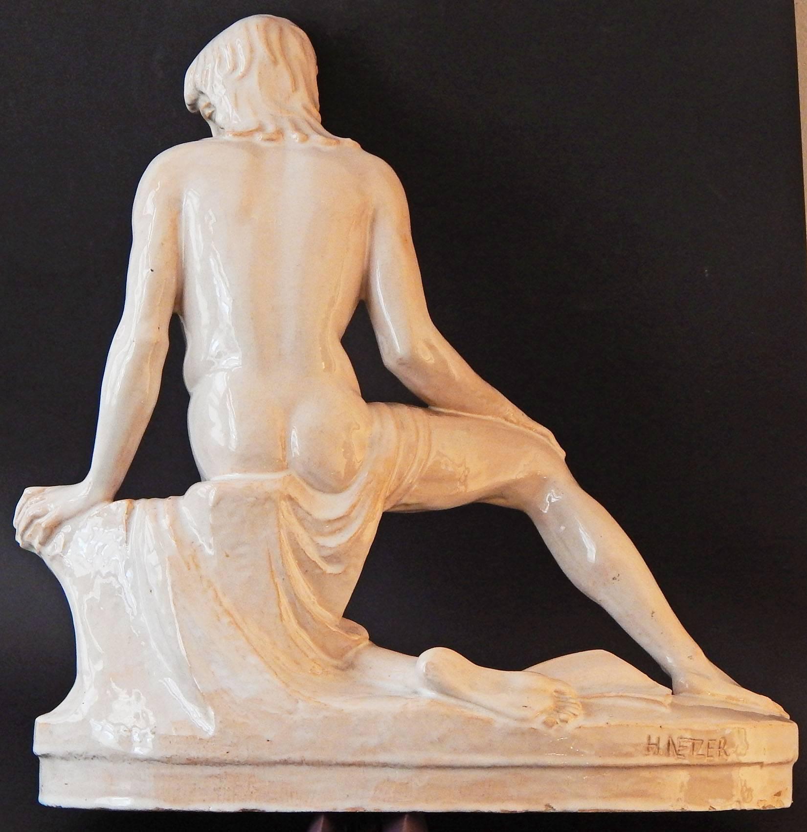 This unique sculpture -- carved and shaped in a reddish clay, not molded -- depicts a slender nude youth, leaning on a tree stump and looking pensively to one side. The sculpture is bathed in a lovely semi-opaque white glaze, allowing hints of the