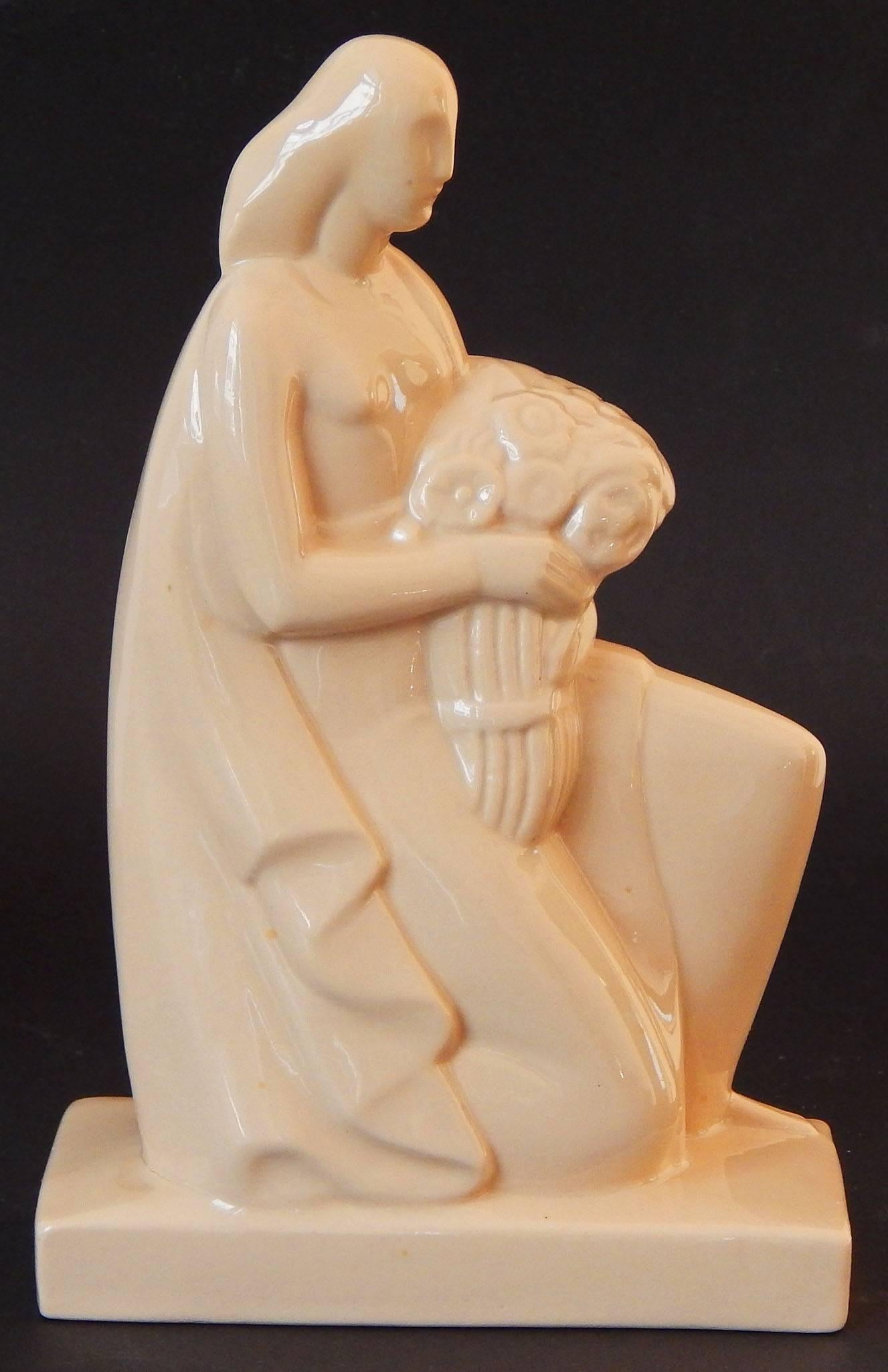 Bathed in a lovely shade of pale caramel, this rare pair of stylized Art Deco sculptures depict female figures holding a scroll in one case, and a bouquet of flowers in the other. The sculptor was Geza De Vegh, an important artist and ceramicist who