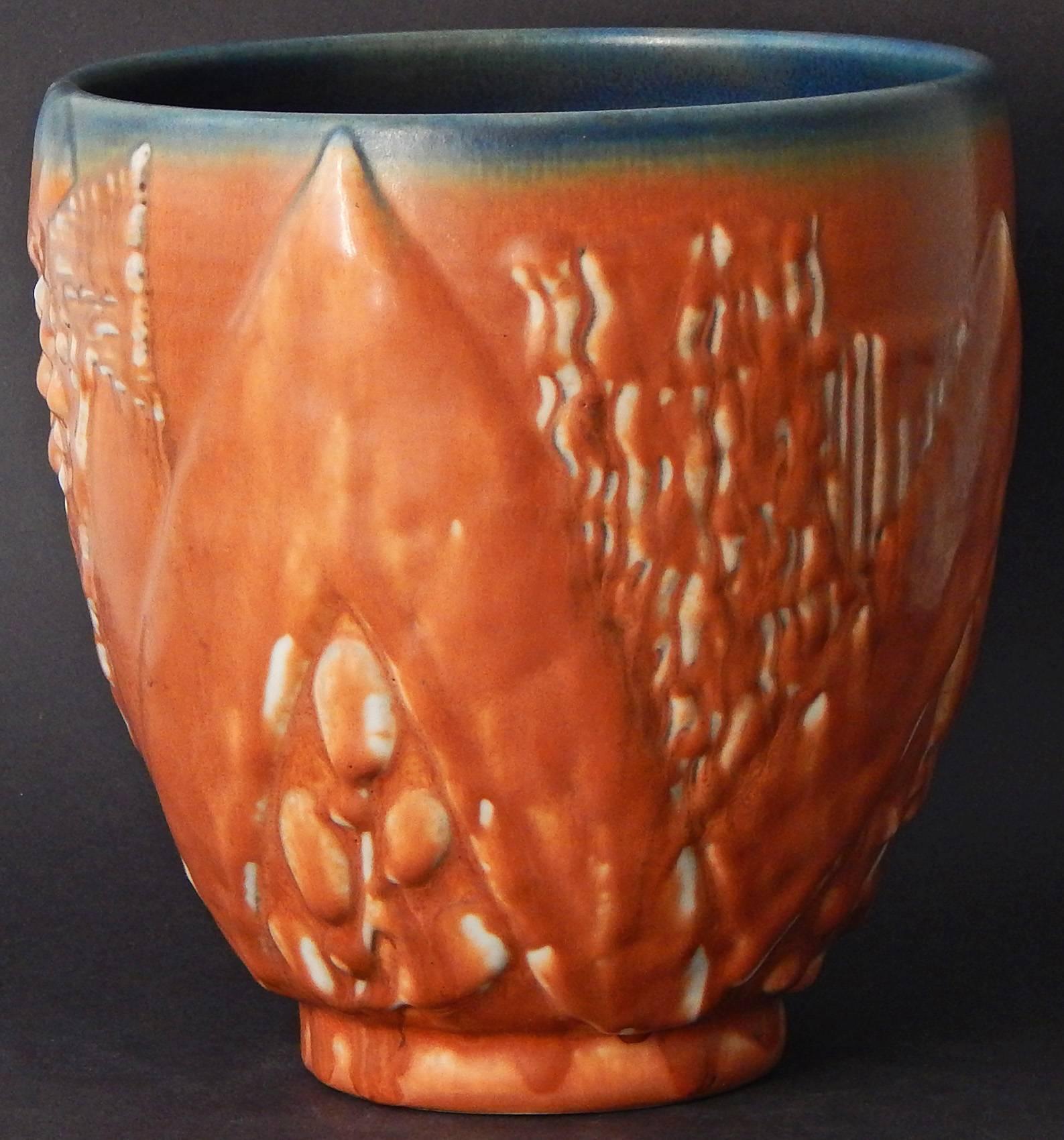 Uno dei più raffinati e notevoli esempi di ceramica Art Déco della famosa ditta Rookwood di Cincinnati, questo vaso splendidamente rifinito con uno smalto color ruggine presenta un pesce scolpito e stilizzato, oltre a grandi motivi chevron. Il vaso