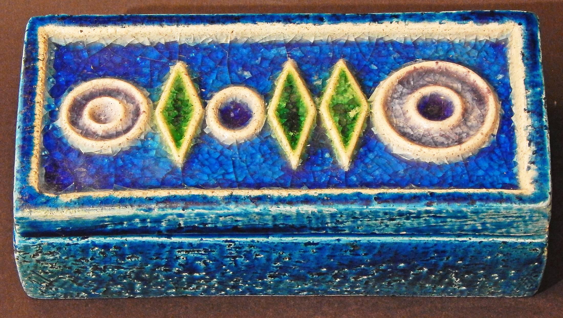 Highly unusual and brilliantly glazed, this covered box features a sequence of geometric shapes in bas relief that are filled with pools of vivid, jewel-toned glazes in sapphire, emerald and amethyst hues. Like Waylande Gregory, the Italian artisan