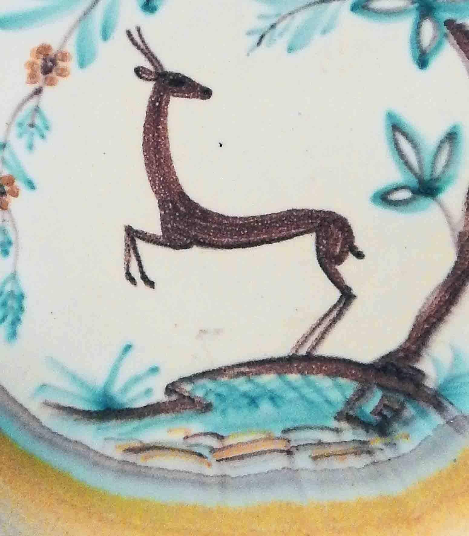 Beautifully glazed in sky blues and golden yellows, this large, low Art Deco bowl features a rearing deer highly stylized in the manner of the period below an arching tree with oversized foliage. This piece was created in Finland, probably in the