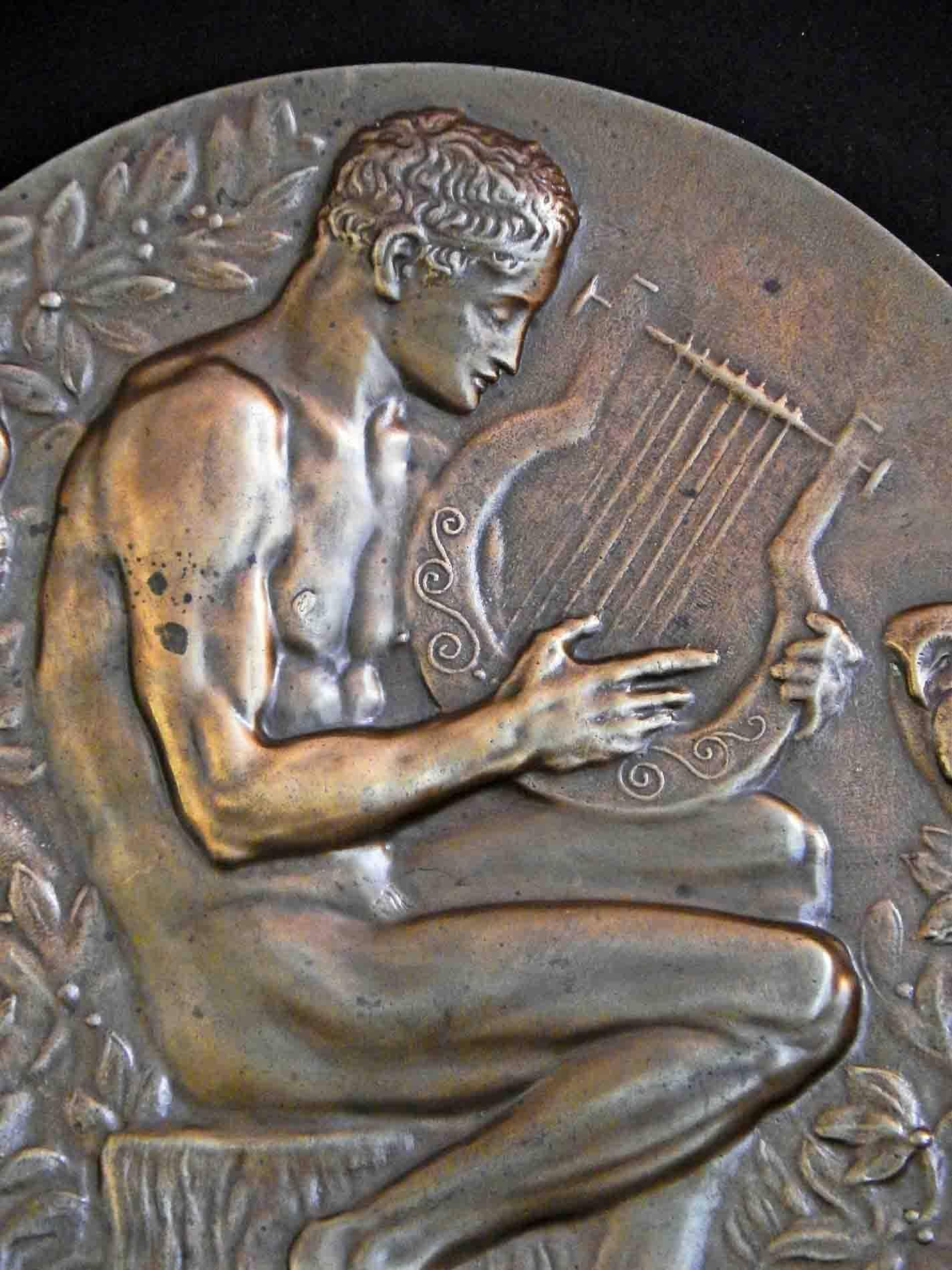 A modern interpretation of the ancient story that Orpheus played the lyre so sweetly and enchantingly that he charmed and calmed wild animals, this Art Deco bronze rondel shows Orpheus with owl and parrot. The nude male figure is beautifully