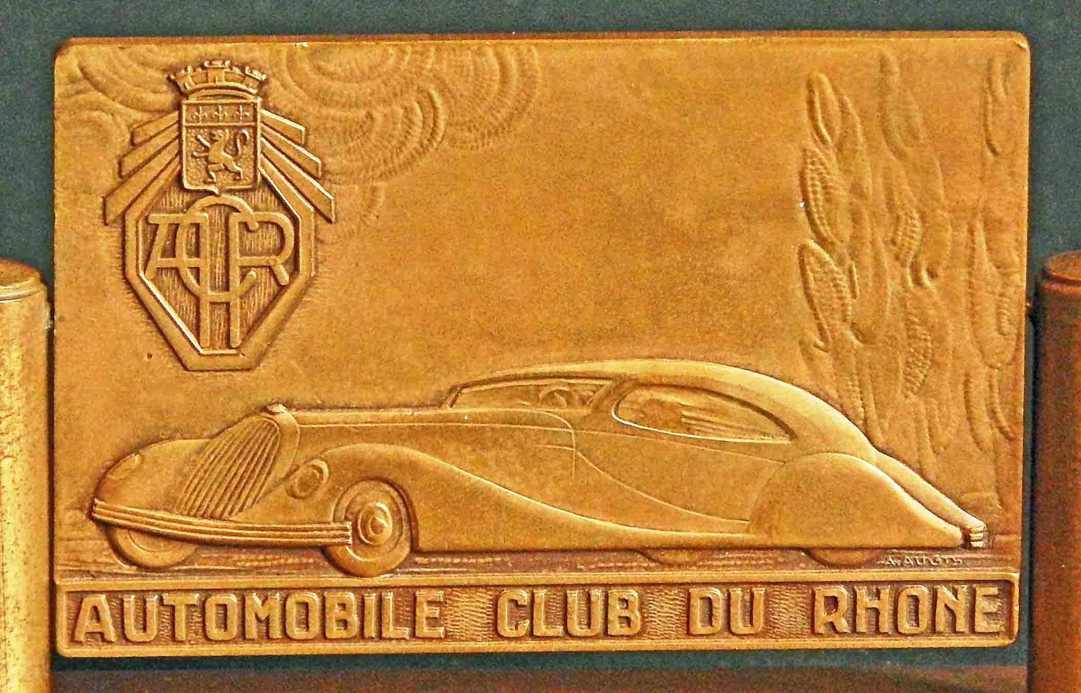 This rare and striking desk accessory, consisting of a bas relief sculptural bronze plaque suspended above a bronze base, was sculpted by A. Augis for the Automobile Club of Rhone, and depicts a streamlined luxury car -- probably a Talbot-Lago coupe