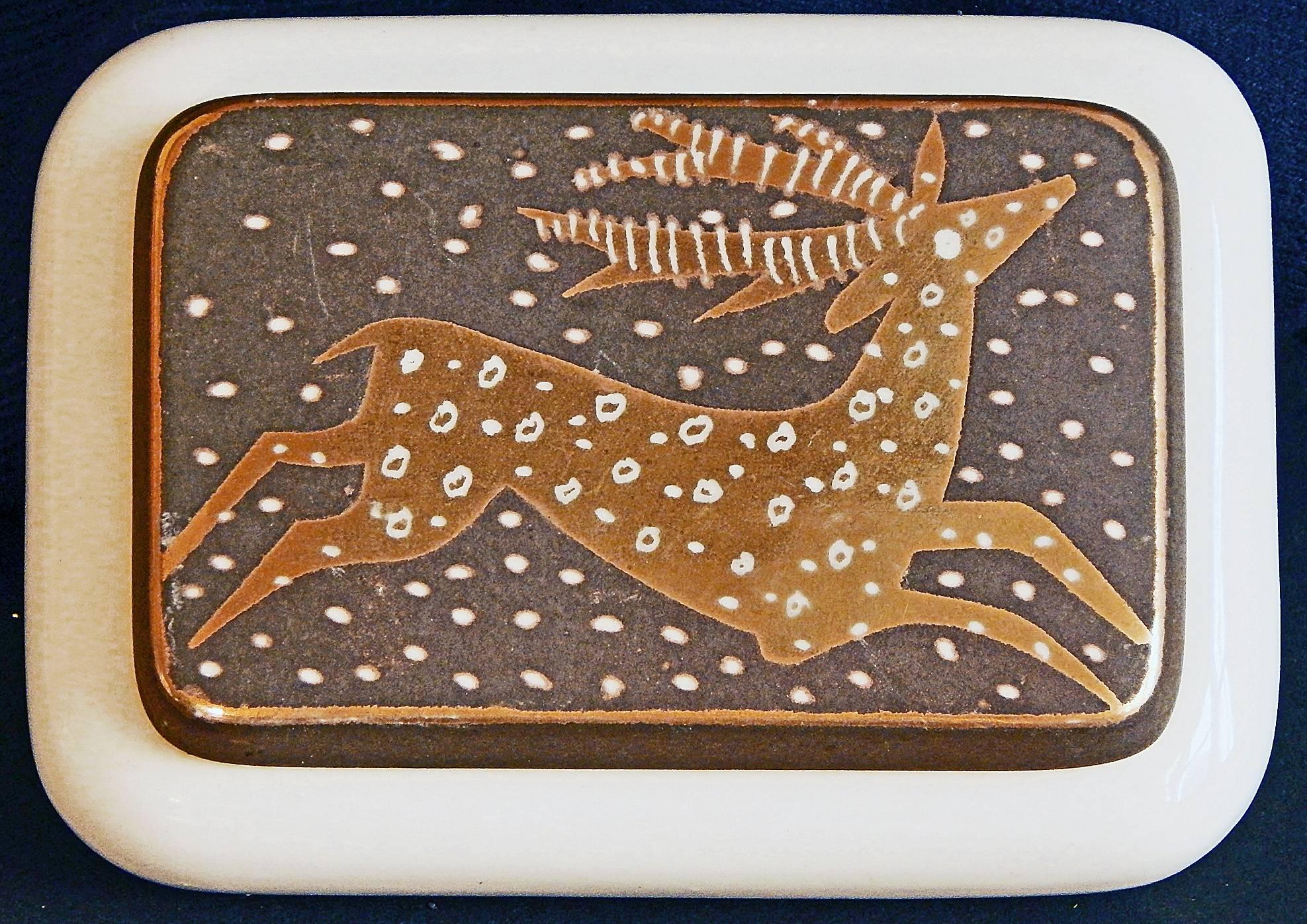 Magnifiquement émaillée dans des tons d'or et de gris foncé chaud, cette boîte en céramique à couvercle représente un cerf bondissant sur son couvercle, les taches sur sa fourrure faisant écho aux gros flocons de neige dans l'air. L'artiste,