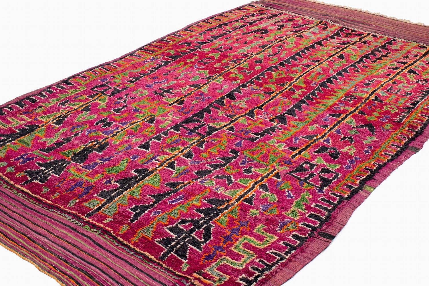 This vibrant one-of-a-kind Moroccan rug has a great vintage feeling. Various shades of magenta, fuchsia and red create the bold field of the rug. Energetic triangles, diamonds and abstract shapes are woven in inky blue, turquoise, lime green, berry
