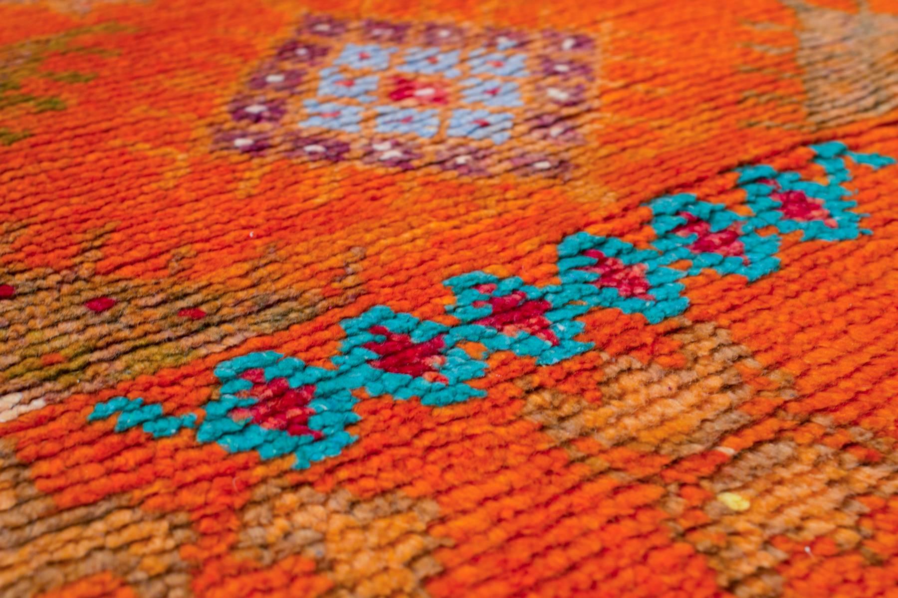 This bright and energetic orange and red vintage Moroccan rug has a short pile and is adorned with beautiful jewel-toned colors. This rug has a border that continues to showcase the representative symbols and design elements throughout. The blue