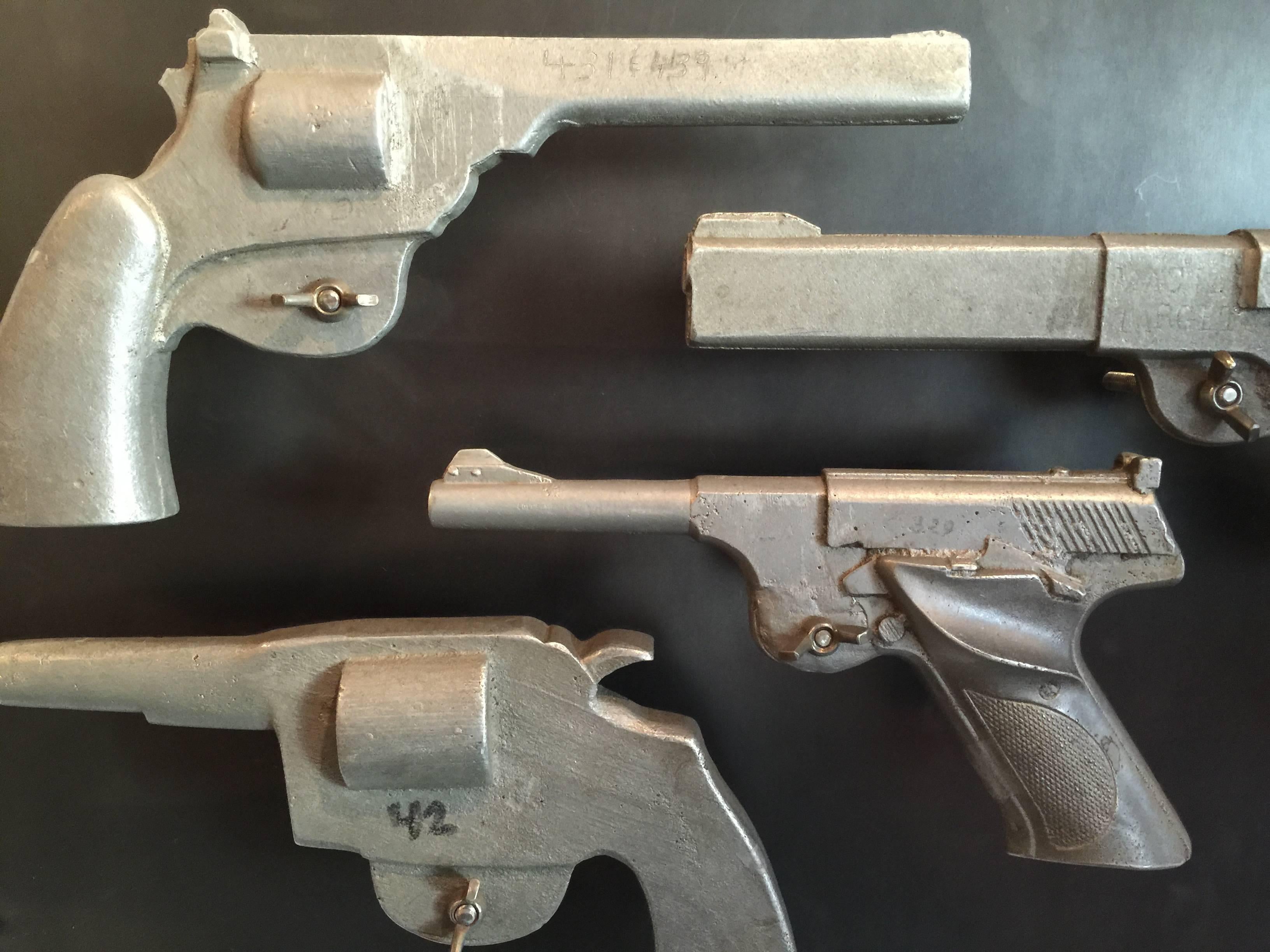 Four cast aluminum pistols which were originally used as weights for molding leather holsters have been mounted onto a steel plate. Each are removable by simply unscrewing the wing nut.
