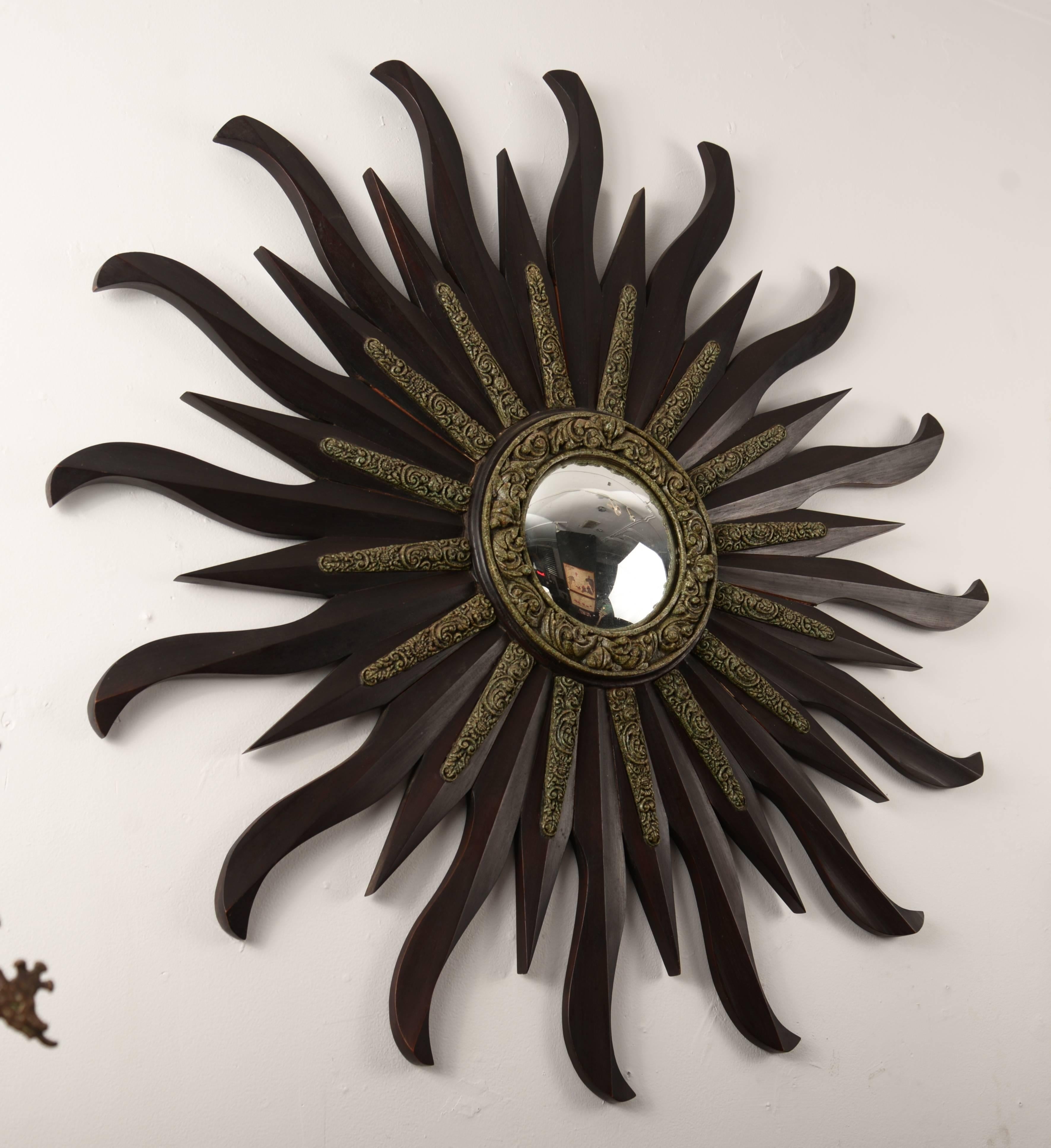 Wooden starburst mirror with a round inset convex mirror and decorative cast tribal ornamentation.
