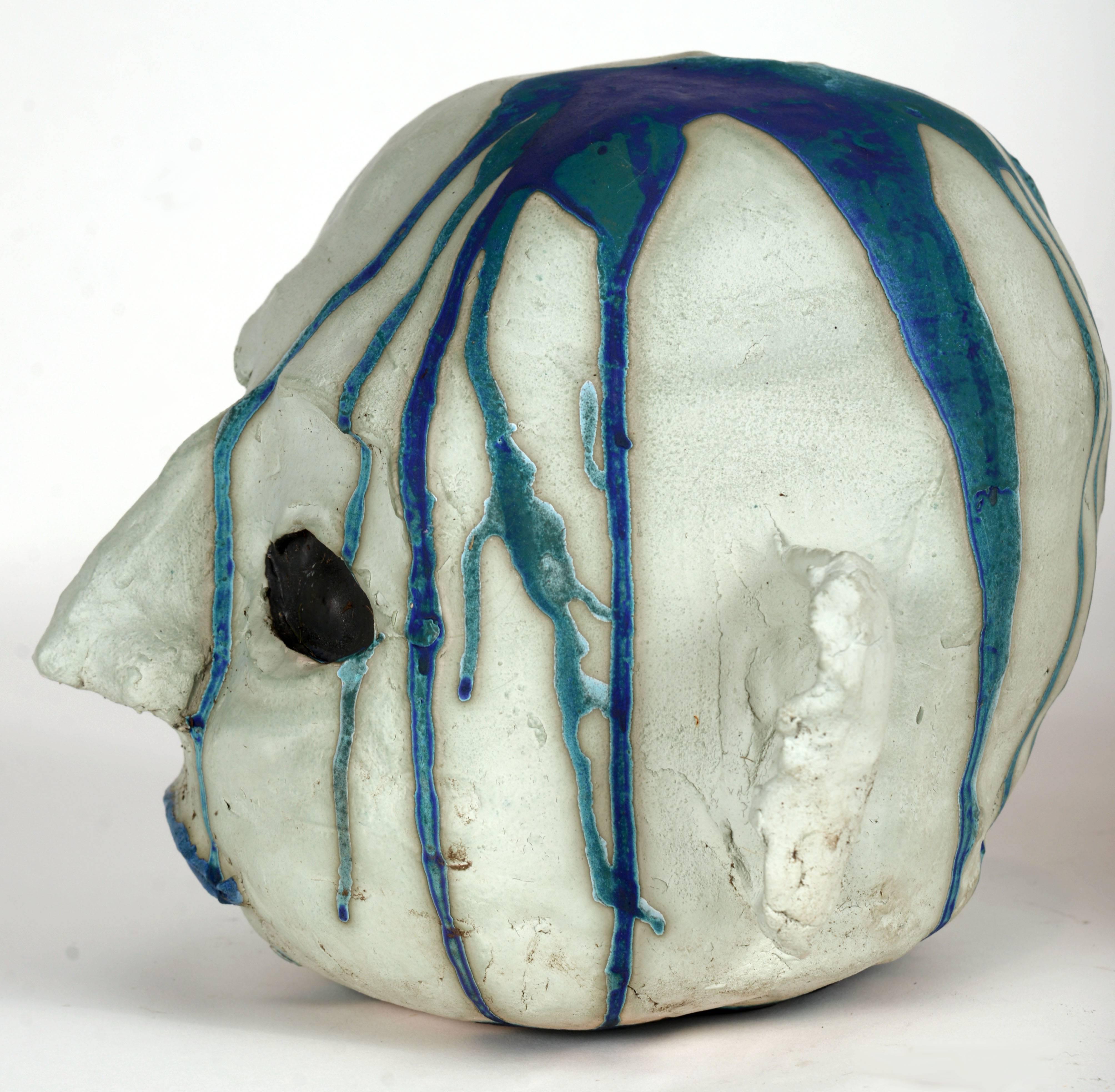 Blue toned ceramic alien head with large black eyes, blue lips and an interesting dual blue glaze pattern running down the right side of his head.