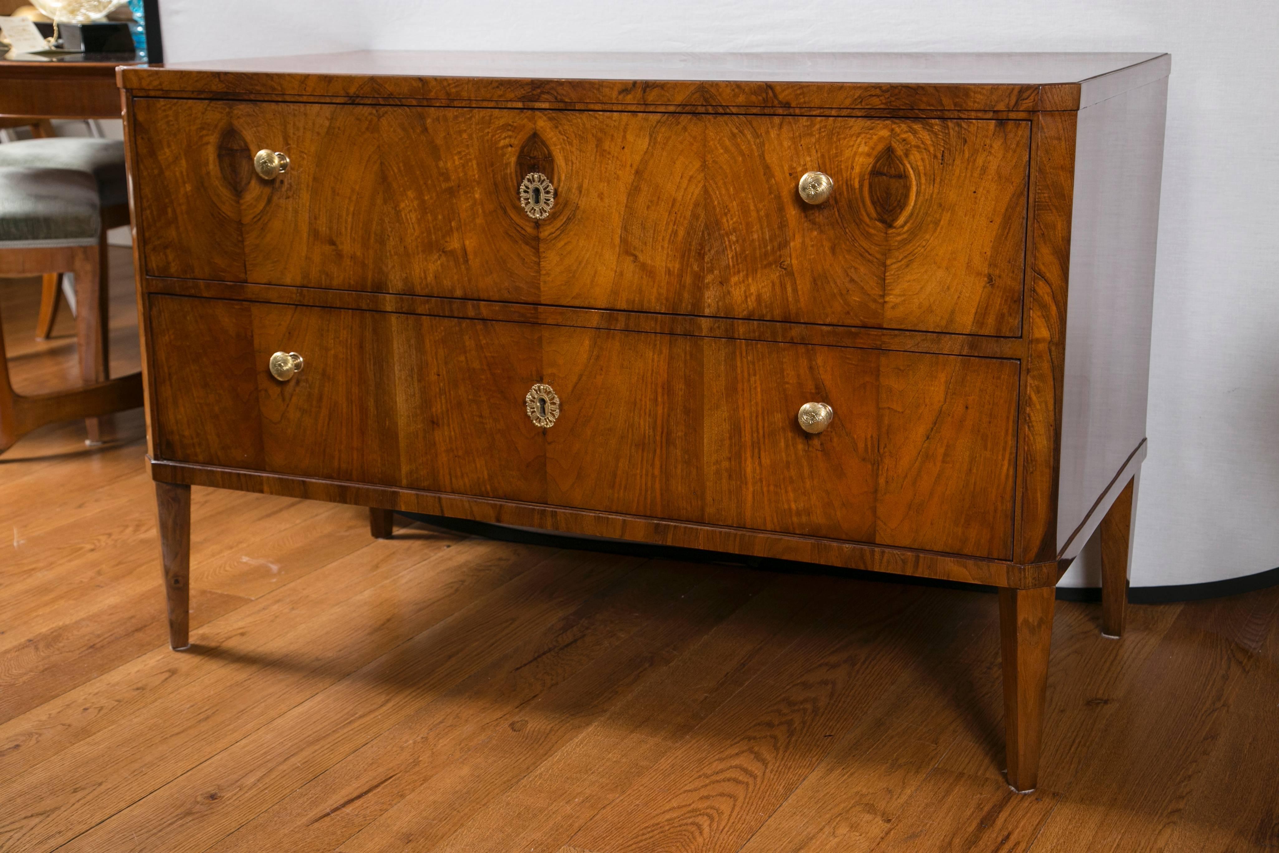 Handsome neoclassical Biedermeier two-drawer chest with chamfered edges and tapering straight legs, gilt brass pulls and escutcheons.
Note lovely movement of the bookmatched walnut veneer.
 