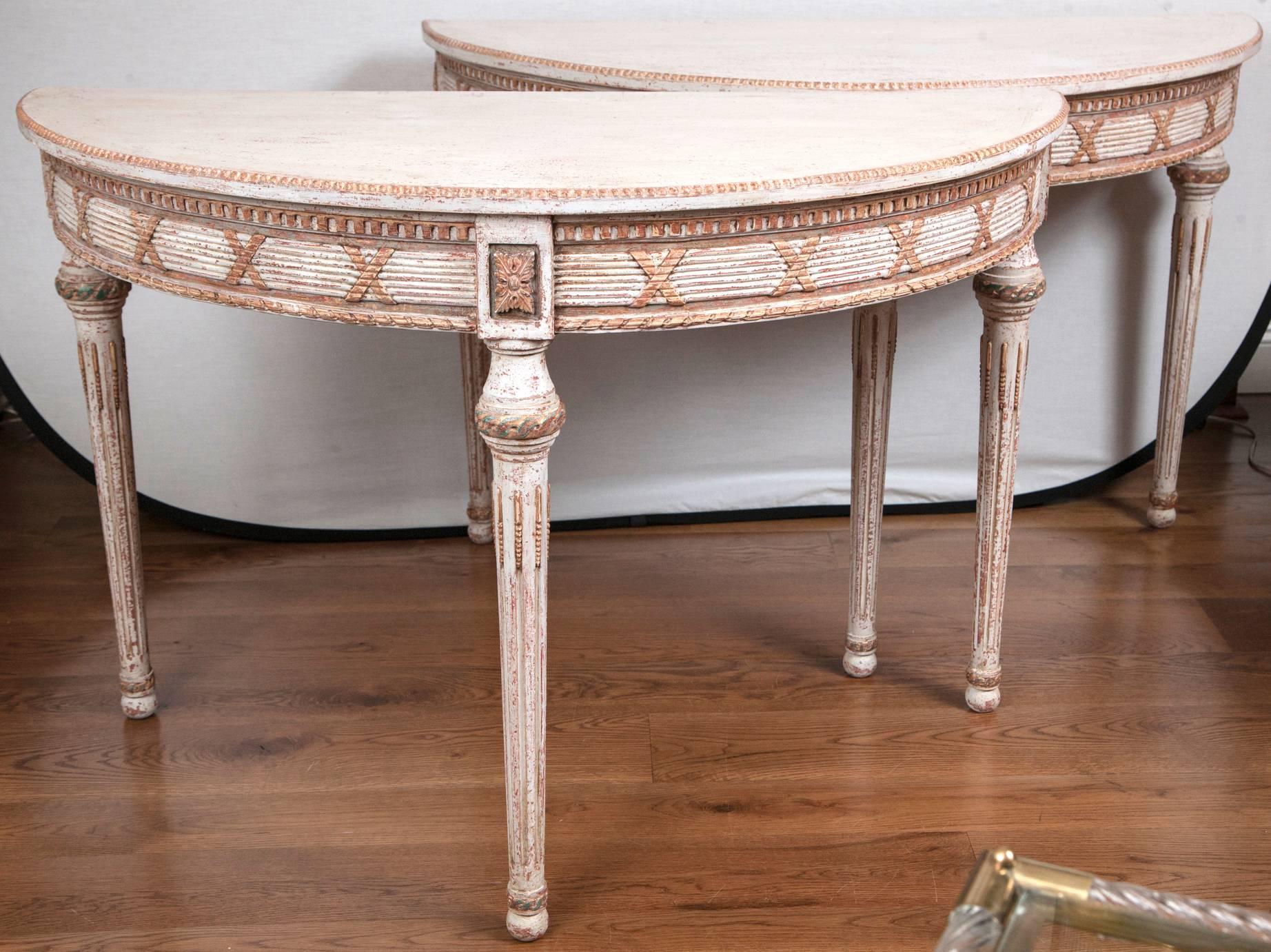 Generously sized pair of neoclassical demilune console tables on three straight and tapered legs adorned with gilded Louis XVI detailing, overall creme color with deep reddish undertones, orginiating from Scandinavia, circa 1890, paint