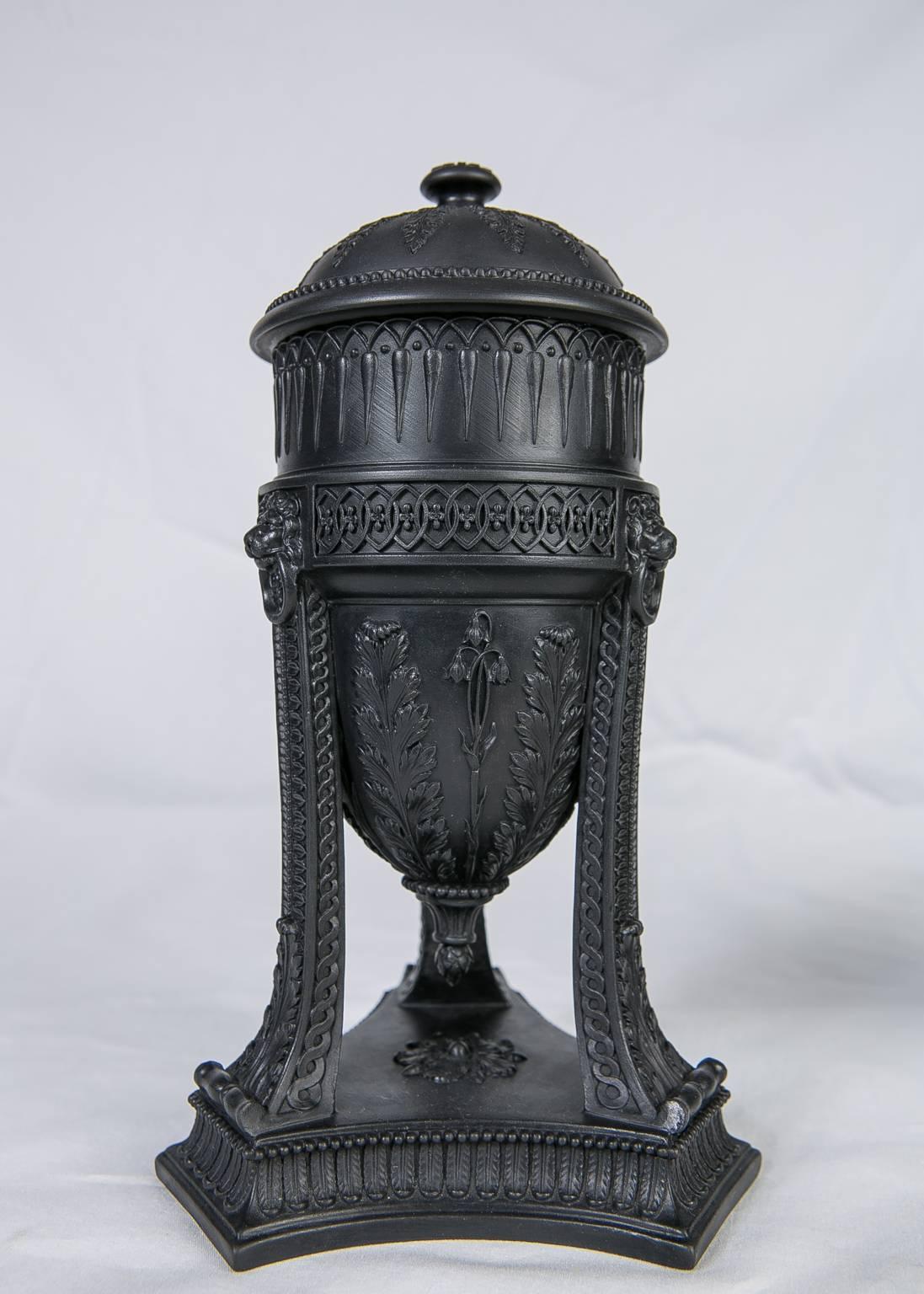 A pair of rare Wedgwood black basalt neoclassical urns made in early 19th century, England. Each urn is raised on a cut cornered tripod base with foliate design of leaf and scrolling vine details.
The handles are in the form of lion's heads.