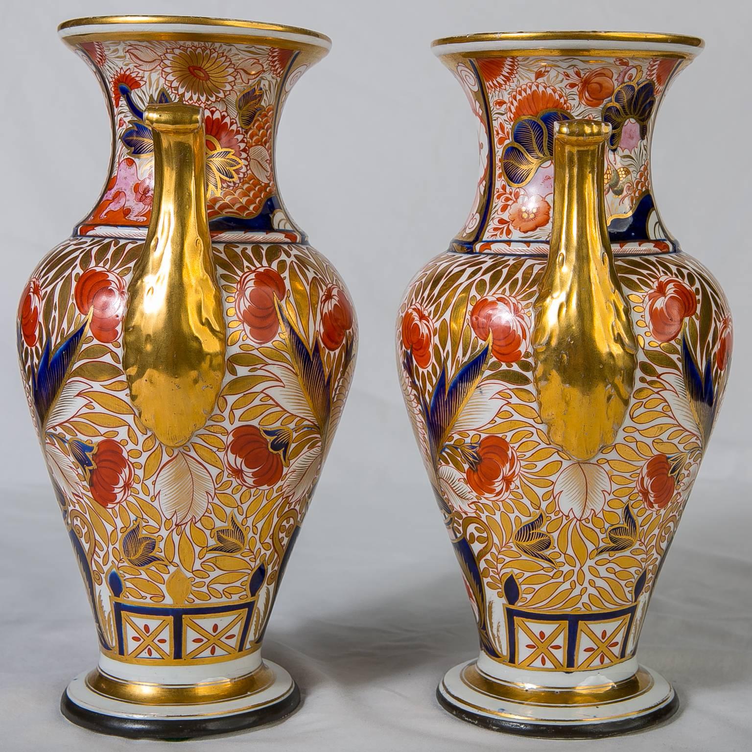 A pair of Coalport vases richly gilded with hand-painted details in cobalt blue, and iron red. The vases are painted in a traditional Imari design. Each vase also has the special design detail of the Coalport 