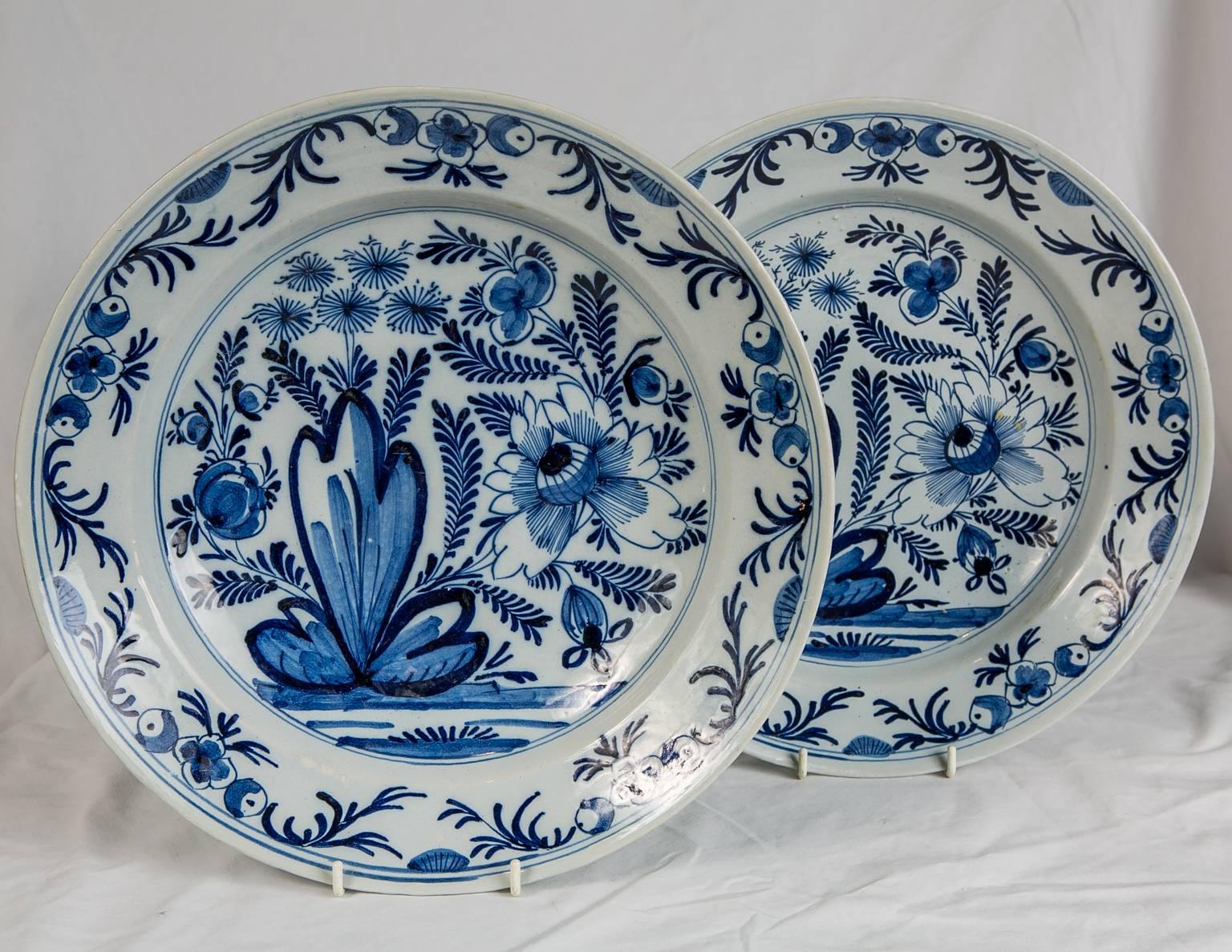 We are pleased to offer this pair of Dutch Delft Blue and White chargers showing a hand-painted cobalt blue garden scene with a large flowering plant, peonies and other flowers. The border is decorated with flowers and scrolling vines. The design is
