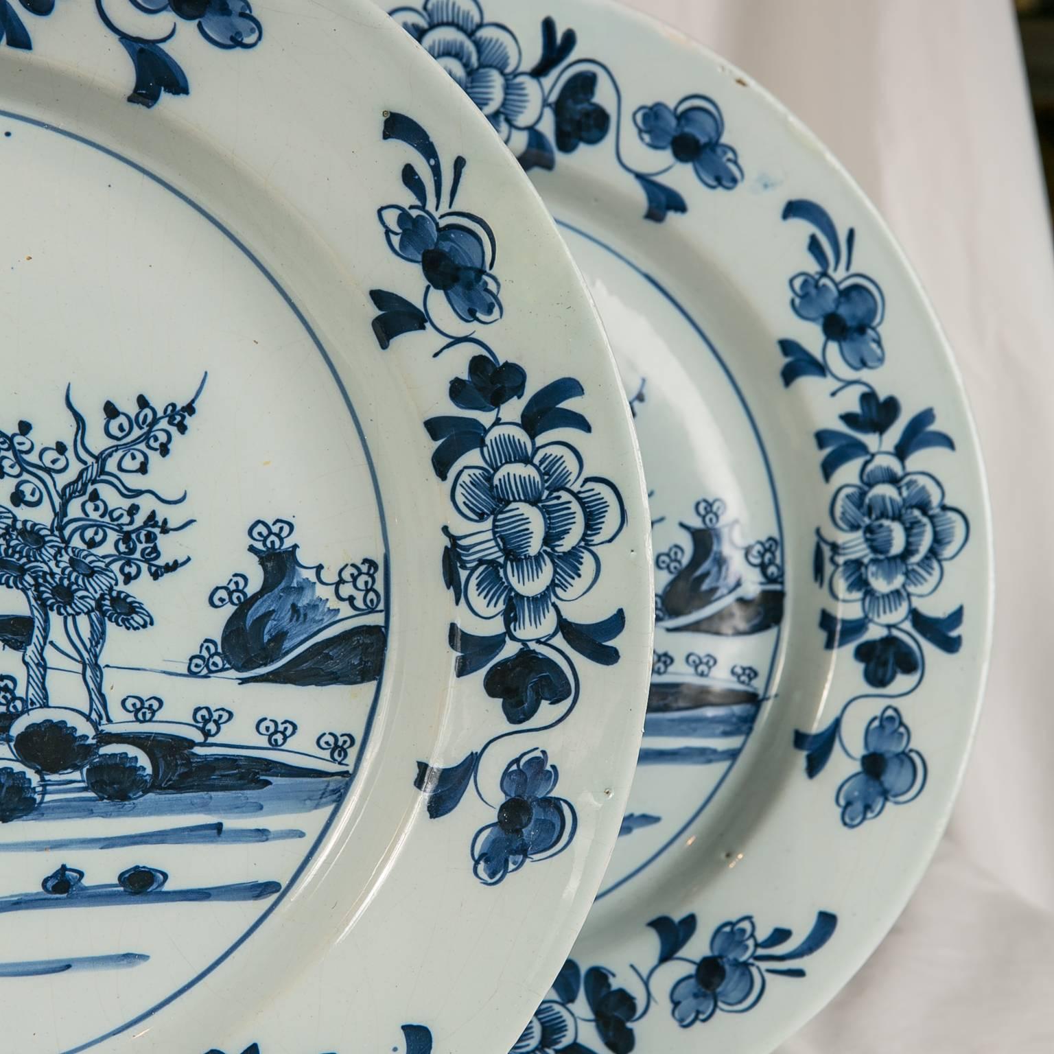 We are pleased to offer this pair of Bristol Delft Blue and White chargers showing a waterside scene with a flowering tree, rocky outcroppings, and birds in flight. The border decorated with flowers and scrolling vines. This pair of Delft chargers
